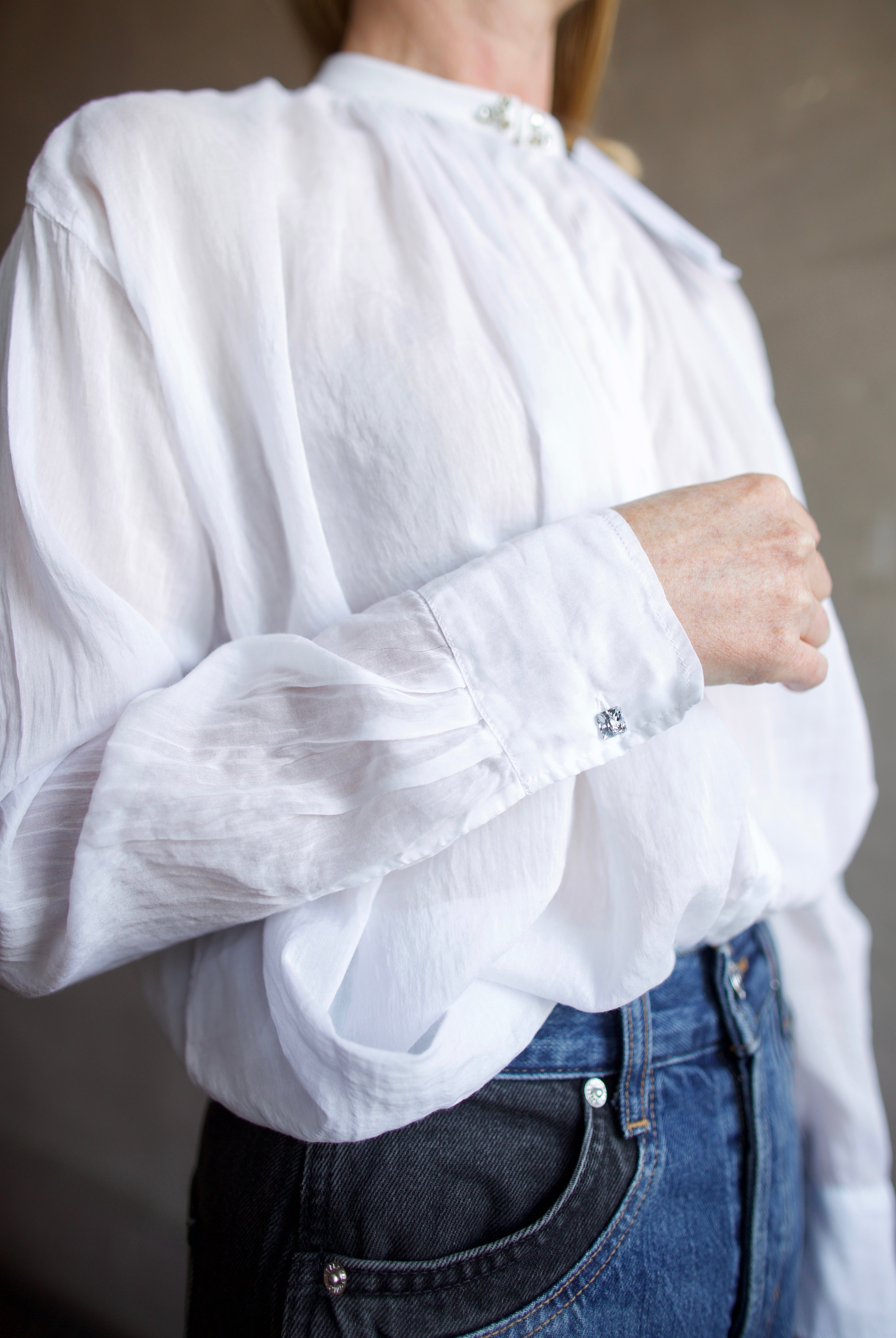 Image featuring a woman wearing the voile bohemian shirt by Forte Forte with a hook and eye closure and crystal embellishment at the mandarin collar and sleeve button.