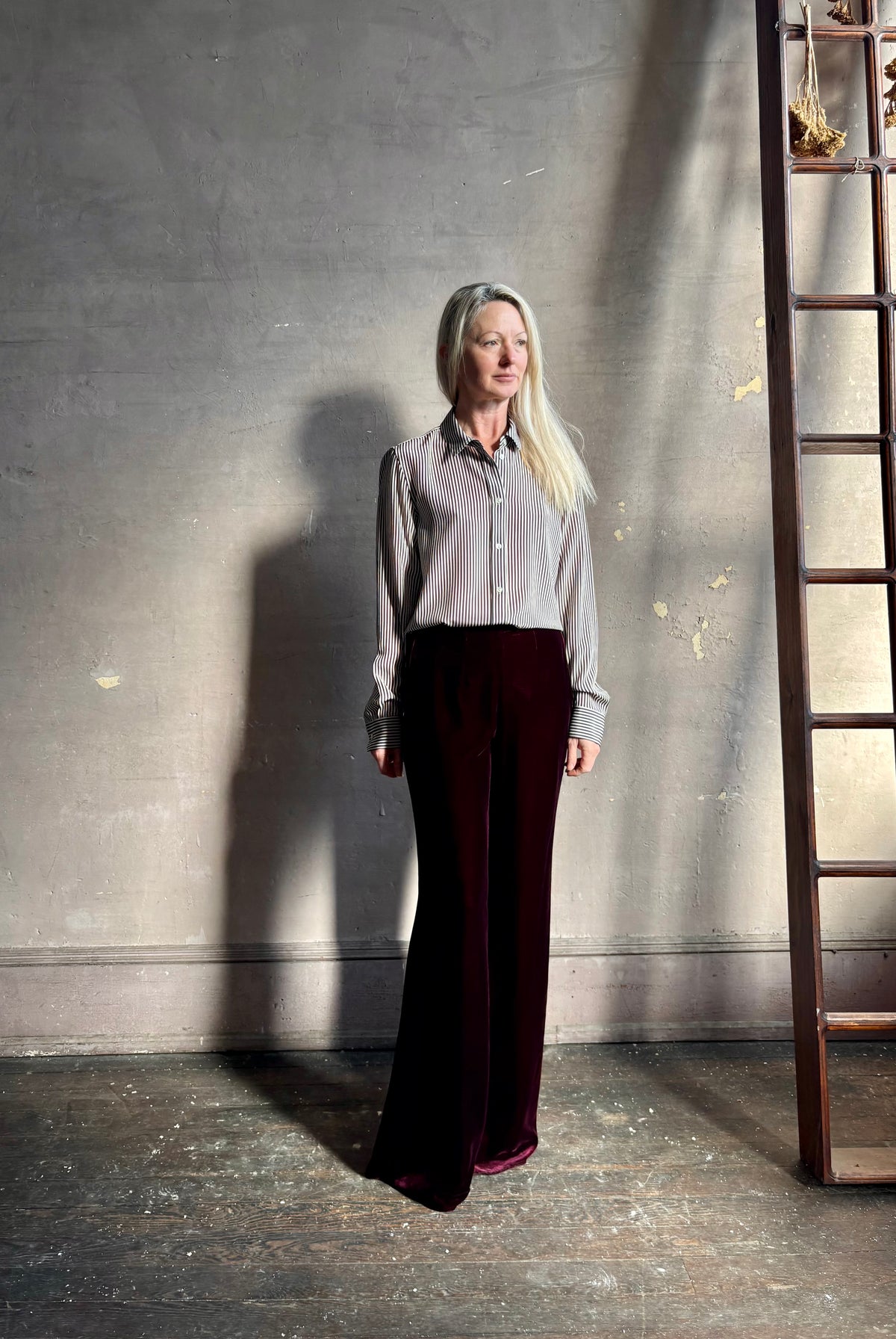 Mature woman wearing dark burgundy velvet Italian made flared trousers from Forte Forte