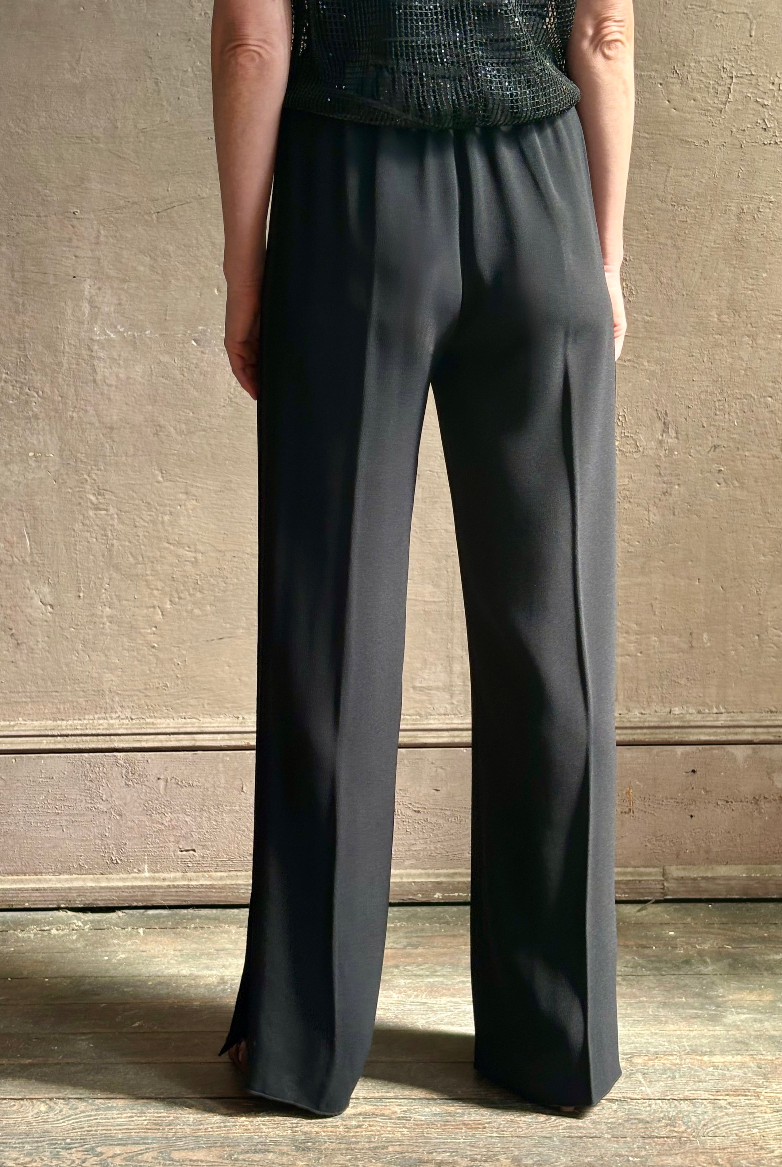 Mature model wearing luxury Italian designer Forte Forte black wide-leg pull on pants with satin tuxedo side stripe and bottom slit