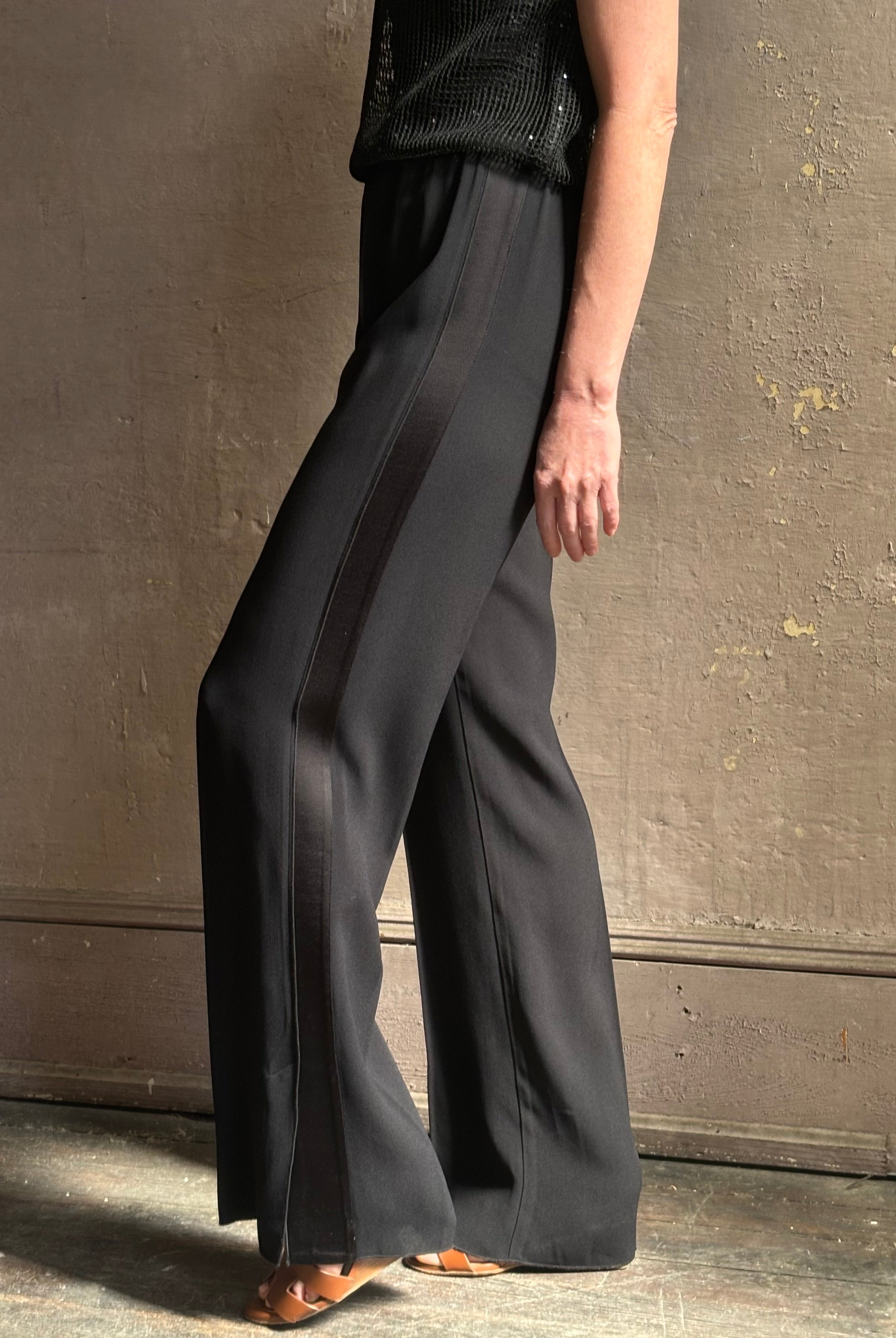 Mature model wearing luxury Italian designer Forte Forte black wide-leg pull on pants with satin tuxedo side stripe and bottom slit