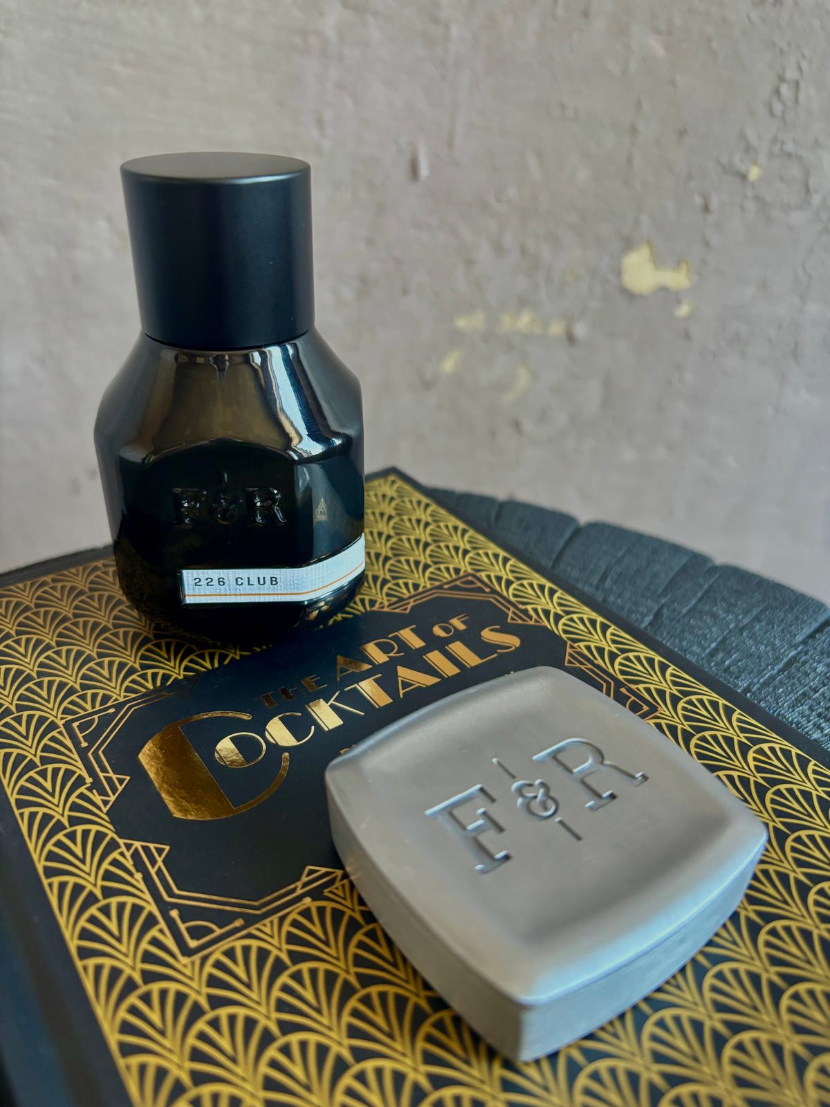 A black bottle of extrait de parfum 226 CLUB and a square metallic silver solid scent designed to evoke a 1920's speak easy