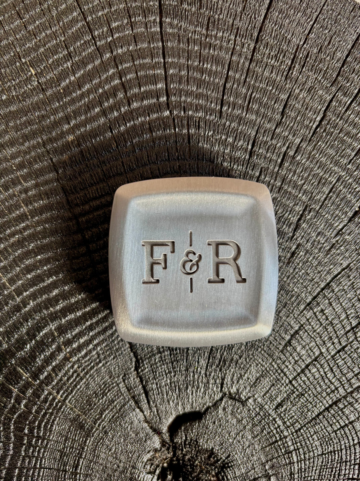 A square metal holder with rounded corners and the embossed initials 'F&R' in the center that comes with one well of solid Matia personal fragrance refillable. made in USA
