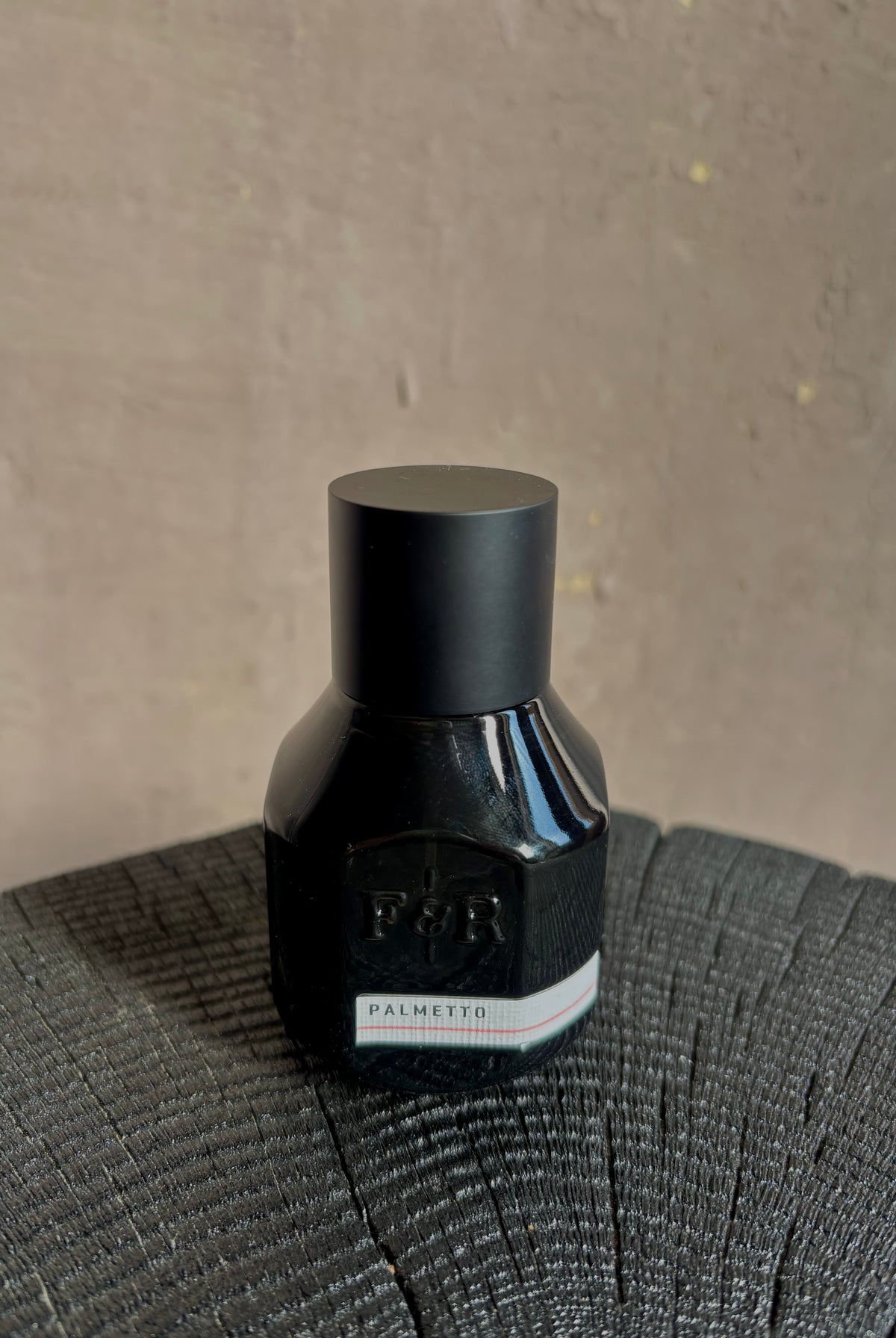 Image of small black bottle with a matte black metal cap and a white label reading PALMETTO and F&R Monogramed Extrait de Parfum made in USA