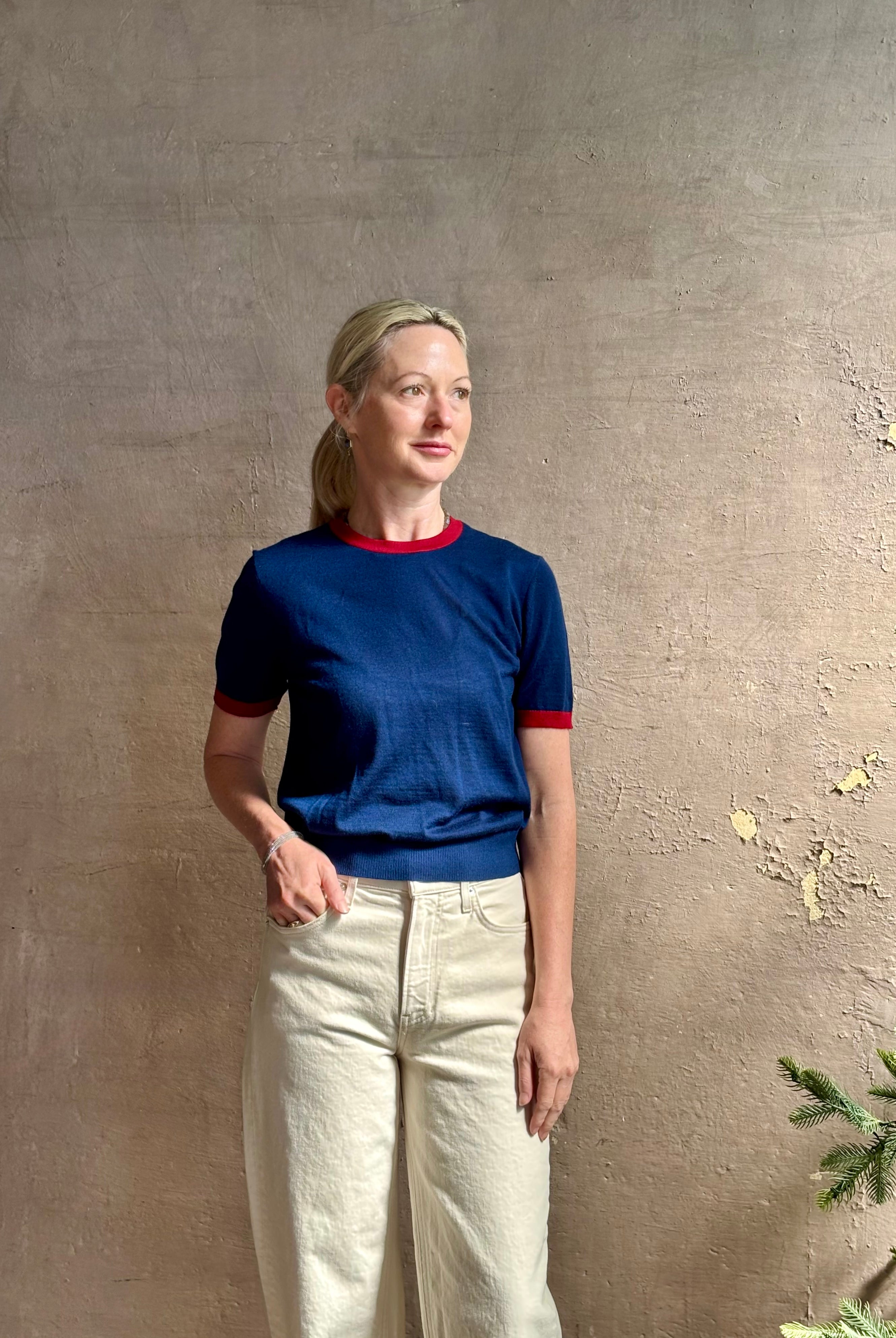Mature woman wearing women's designer cashmere Airy short sleeve Ringer Tee from Guest in Residence rendered in a navy body with carmine ringer detailing and crafted from 100% lightweight cashmere with a crew neckline
