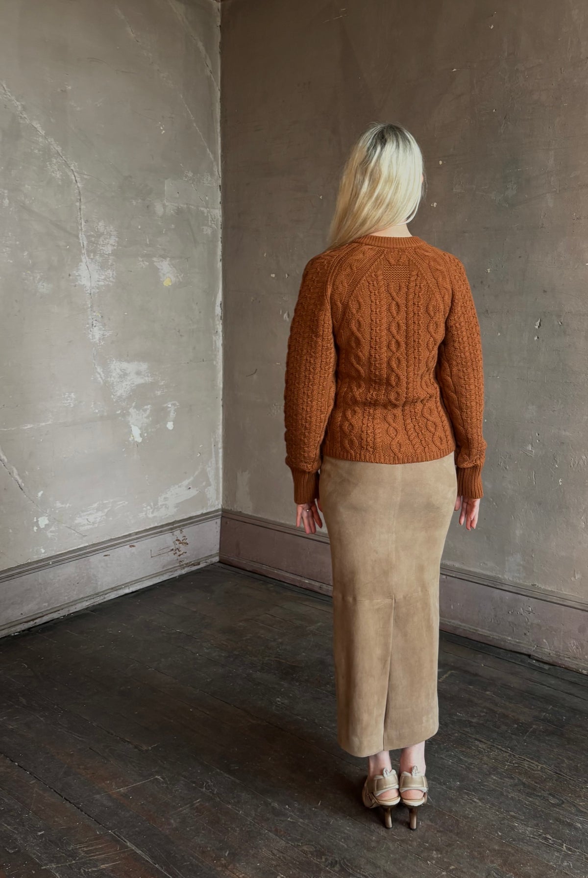 Mature woman wearing Guest in Residence's Cable Sculpted Cardigan Burnt Sienna wool-cashmere cable knit raglan sleeves. Richly textured heirloom-quality warmth