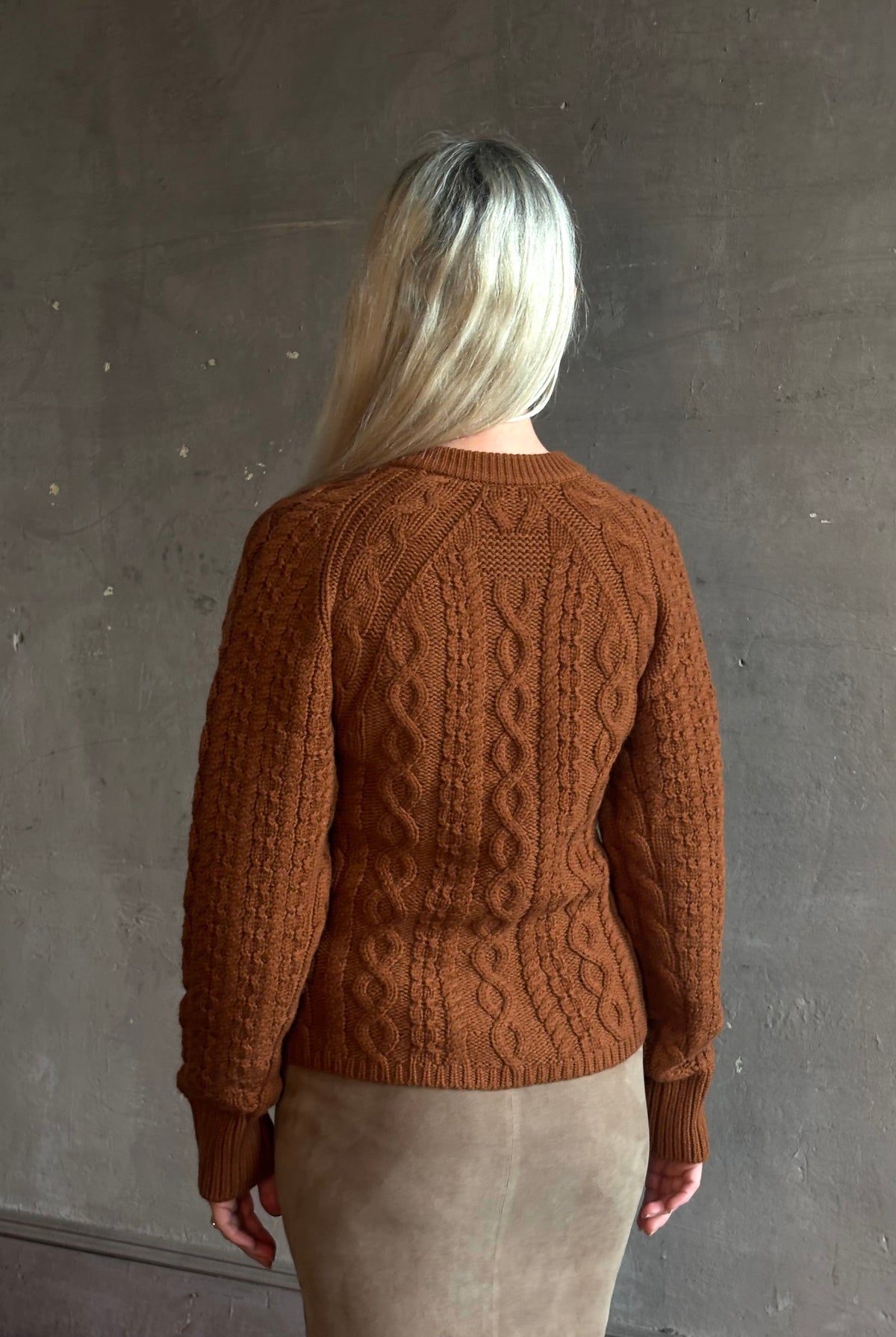 Mature woman wearing Guest in Residence's Cable Sculpted Cardigan Burnt Sienna wool-cashmere cable knit raglan sleeves. Richly textured heirloom-quality warmth