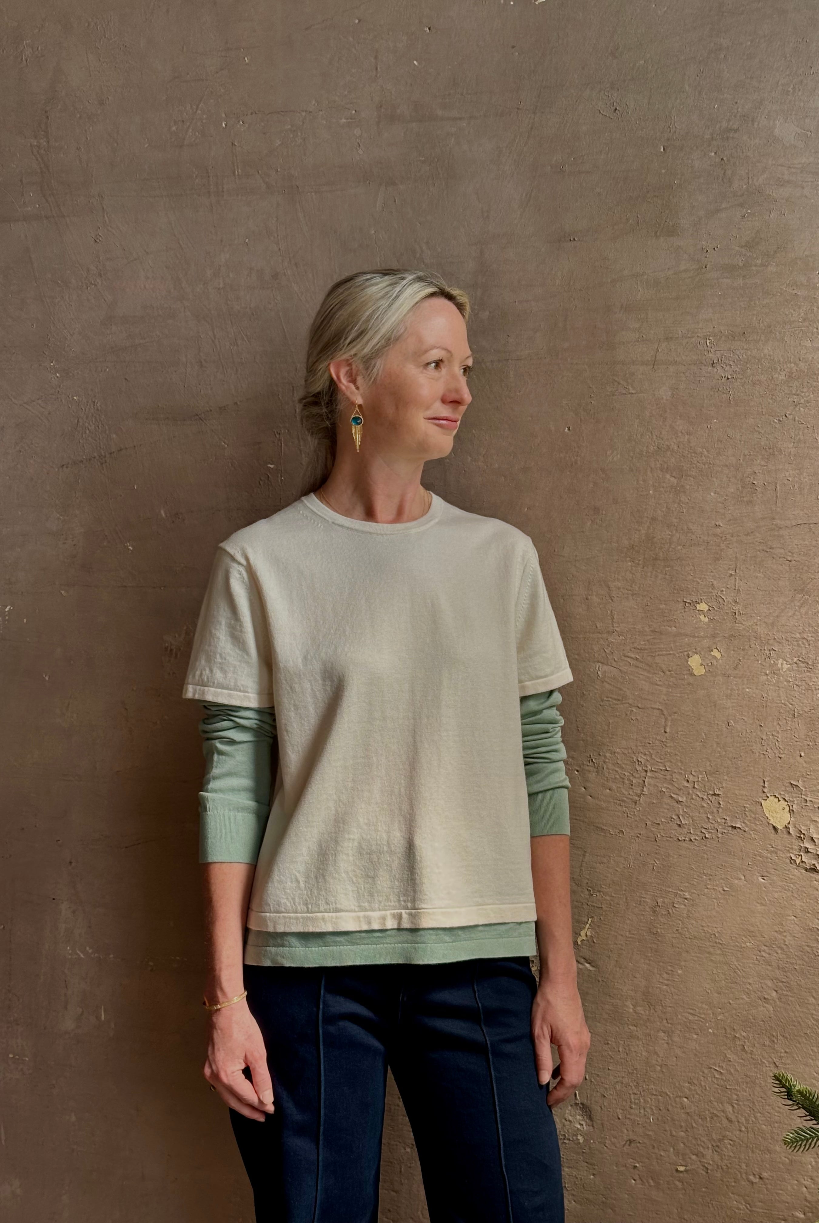 Mature woman wearing elevated luxury Layer Tee Shirt from Guest in Residence rendered in a soft sage brush green and cream colorway and crafted from an exceptional blend of cotton, cashmere, and silk with long sleeves and a crew neckline