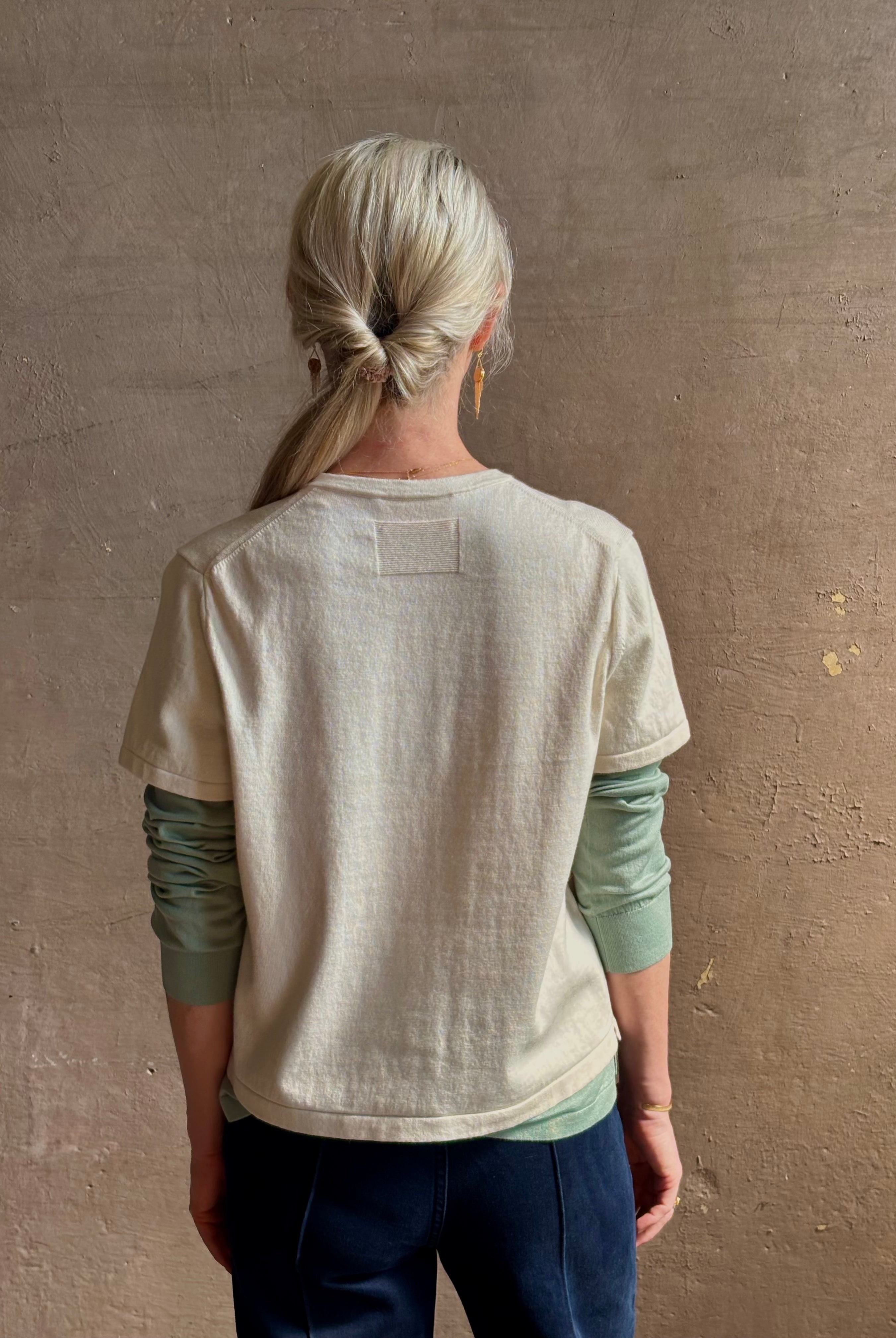 Mature woman wearing elevated luxury Layer Tee Shirt from Guest in Residence rendered in a soft sage brush green and cream colorway and crafted from an exceptional blend of cotton, cashmere, and silk with long sleeves and a crew neckline