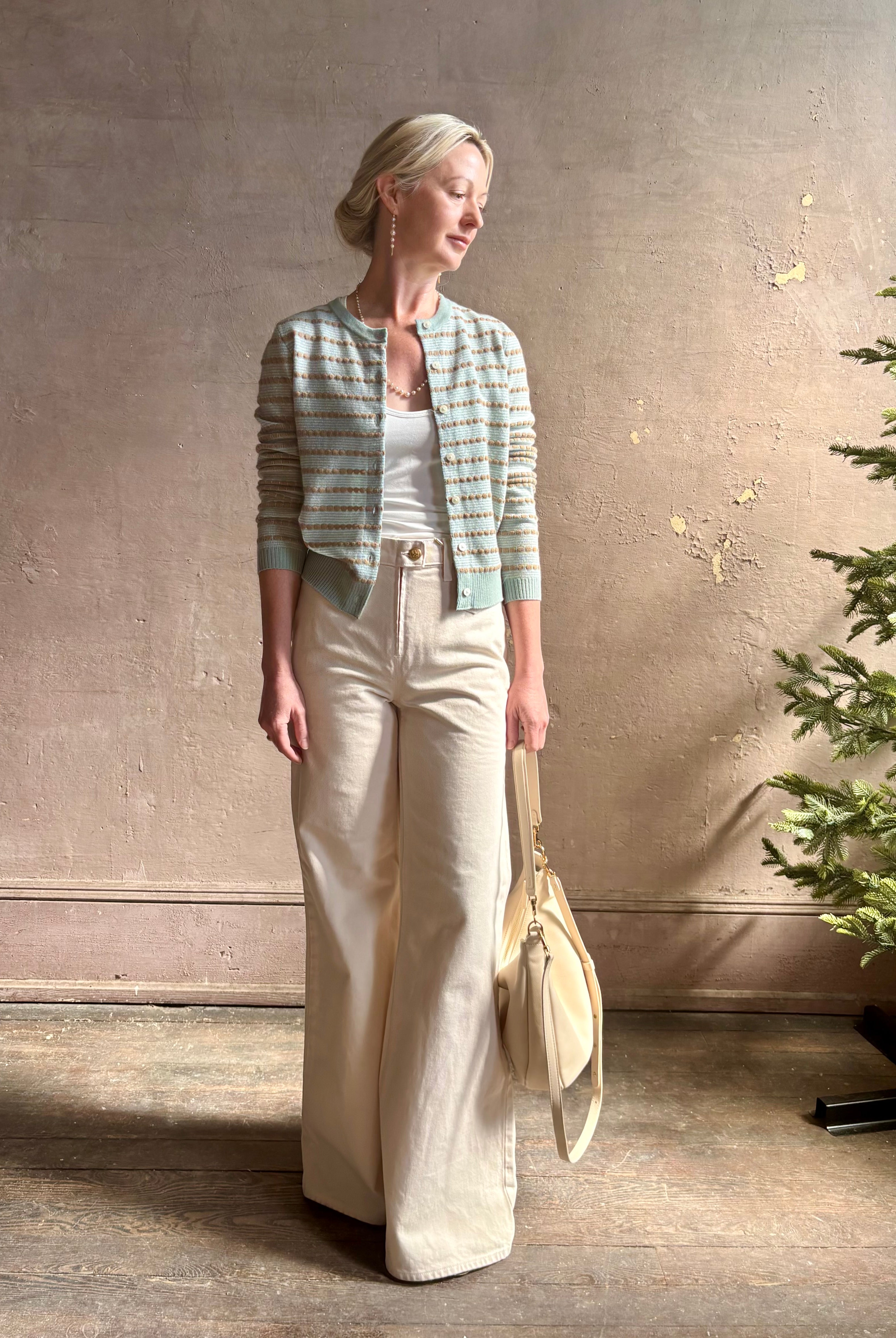 Mature woman wearing Pebble Stripe Jane Cardigan from Guest in Residence rendered in a serene sage brush aqua Khaki combo and crafted from 100% cashmere with crew neck, long sleeves and button front