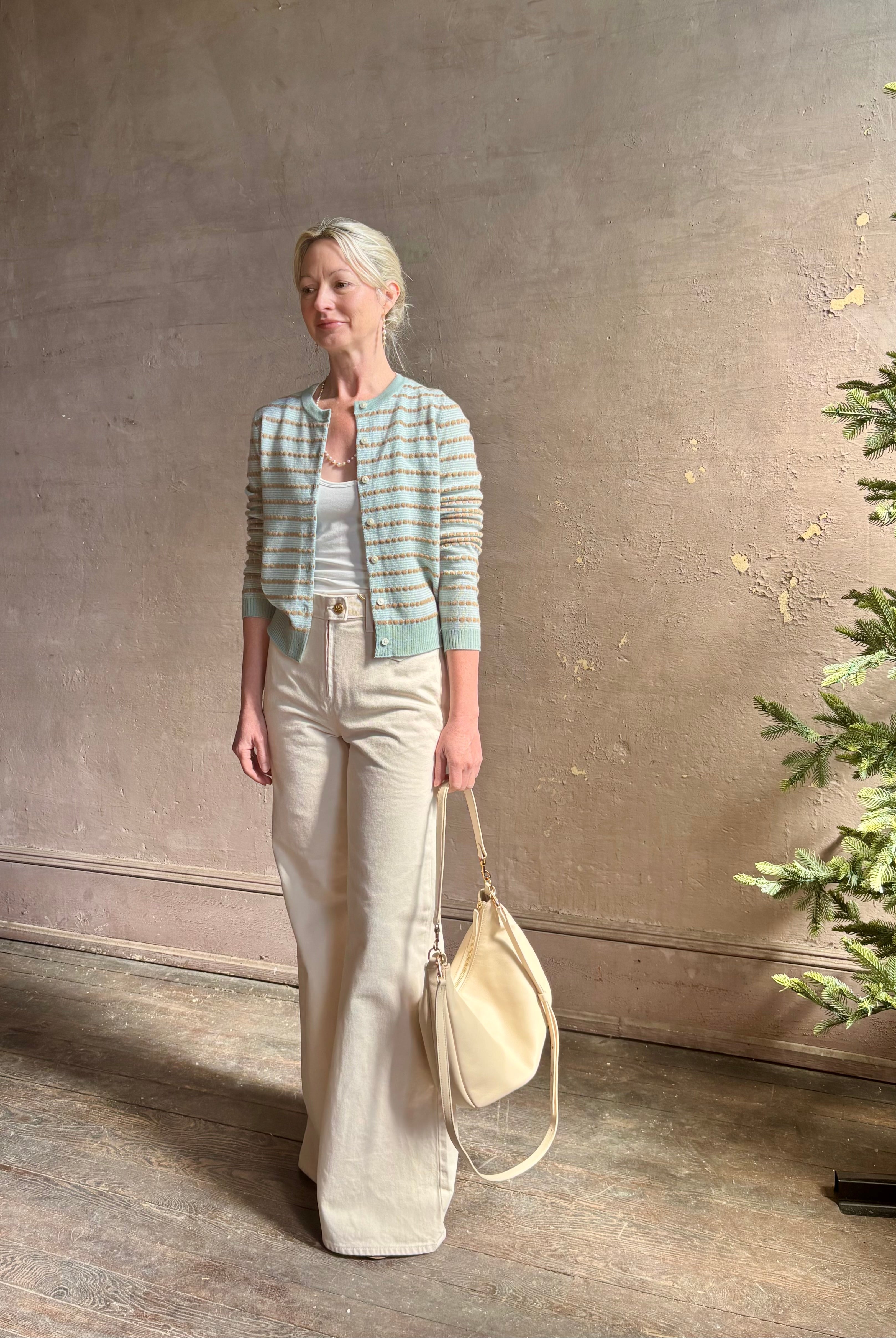 Mature woman wearing Pebble Stripe Jane Cardigan from Guest in Residence rendered in a serene sage brush aqua Khaki combo and crafted from 100% cashmere with crew neck, long sleeves and button front