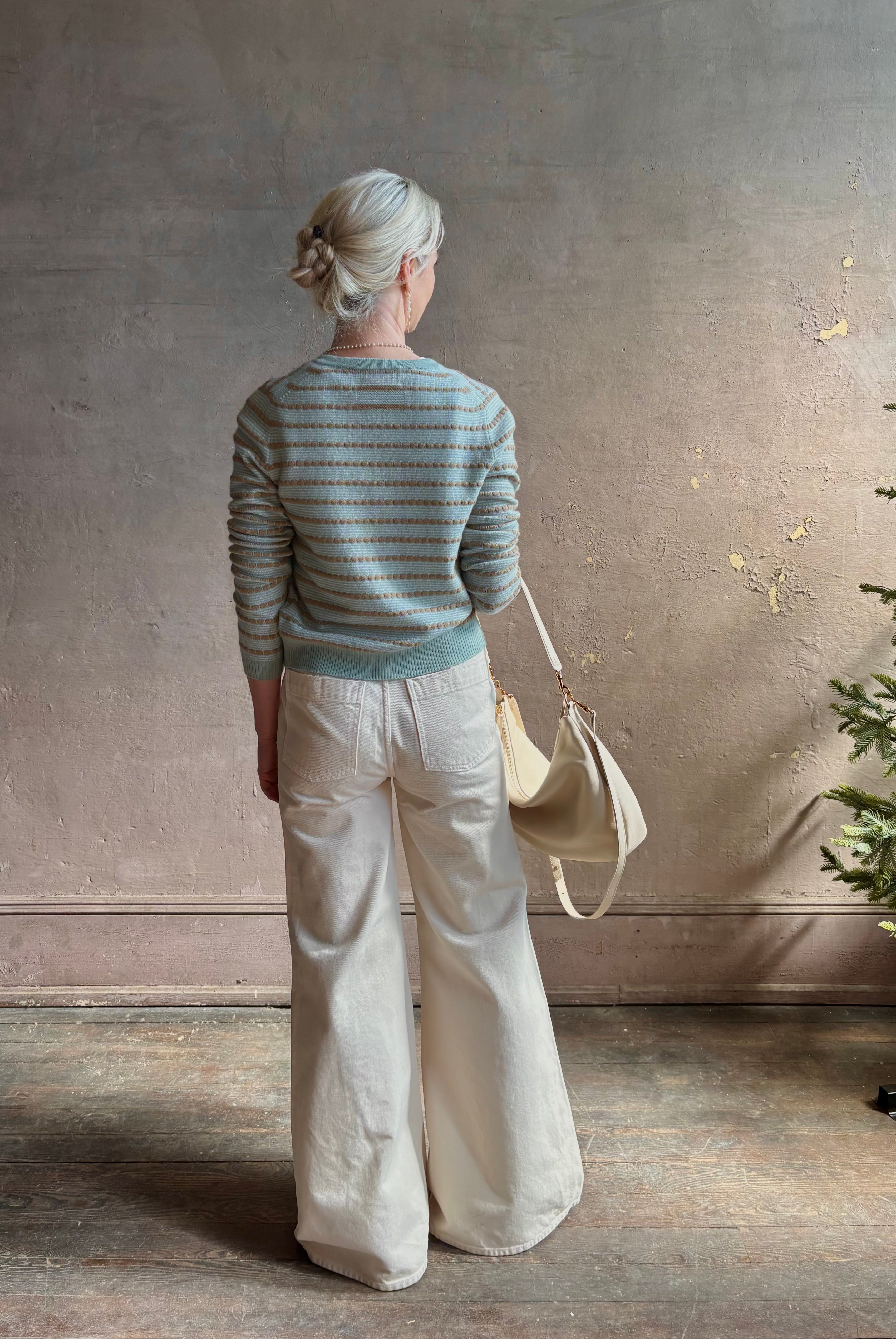 Mature woman wearing Pebble Stripe Jane Cardigan from Guest in Residence rendered in a serene sage brush aqua Khaki combo and crafted from 100% cashmere with crew neck, long sleeves and button front