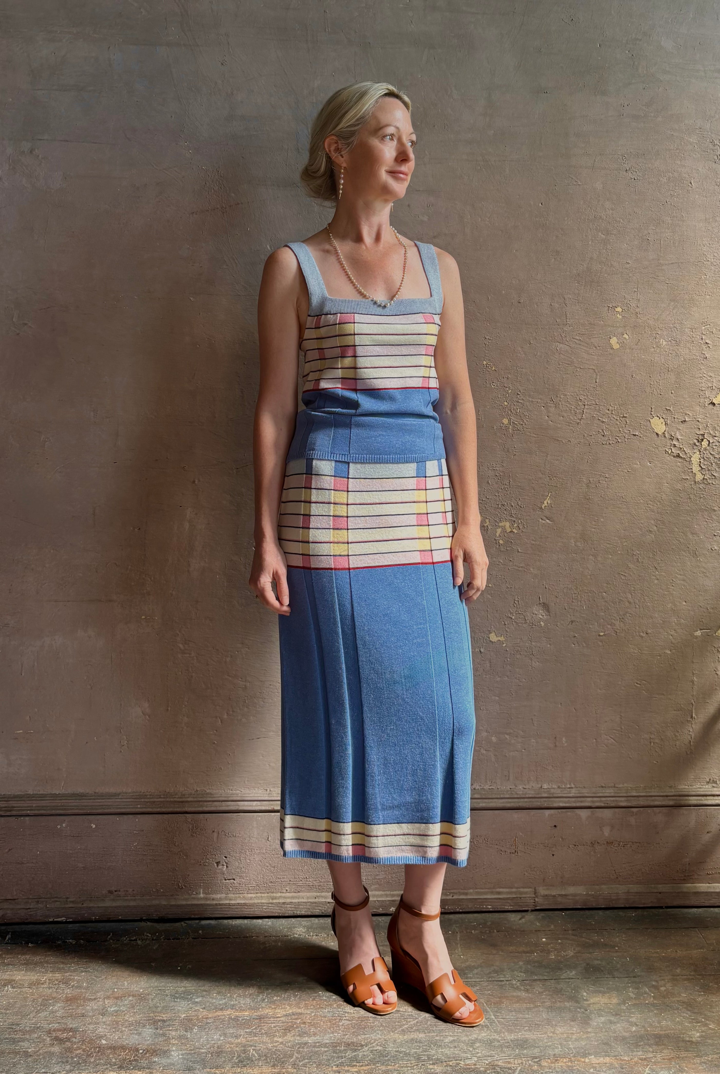 Mature woman wearing Plaited Rib knit pencil Skirt from Guest in Residence rendered in delft blue and crafted from a luxurious blend of silk, linen, nylon, and elastane with wide rib texture down front and back with pink and yellow horizontal stripes at hips and bottom edge