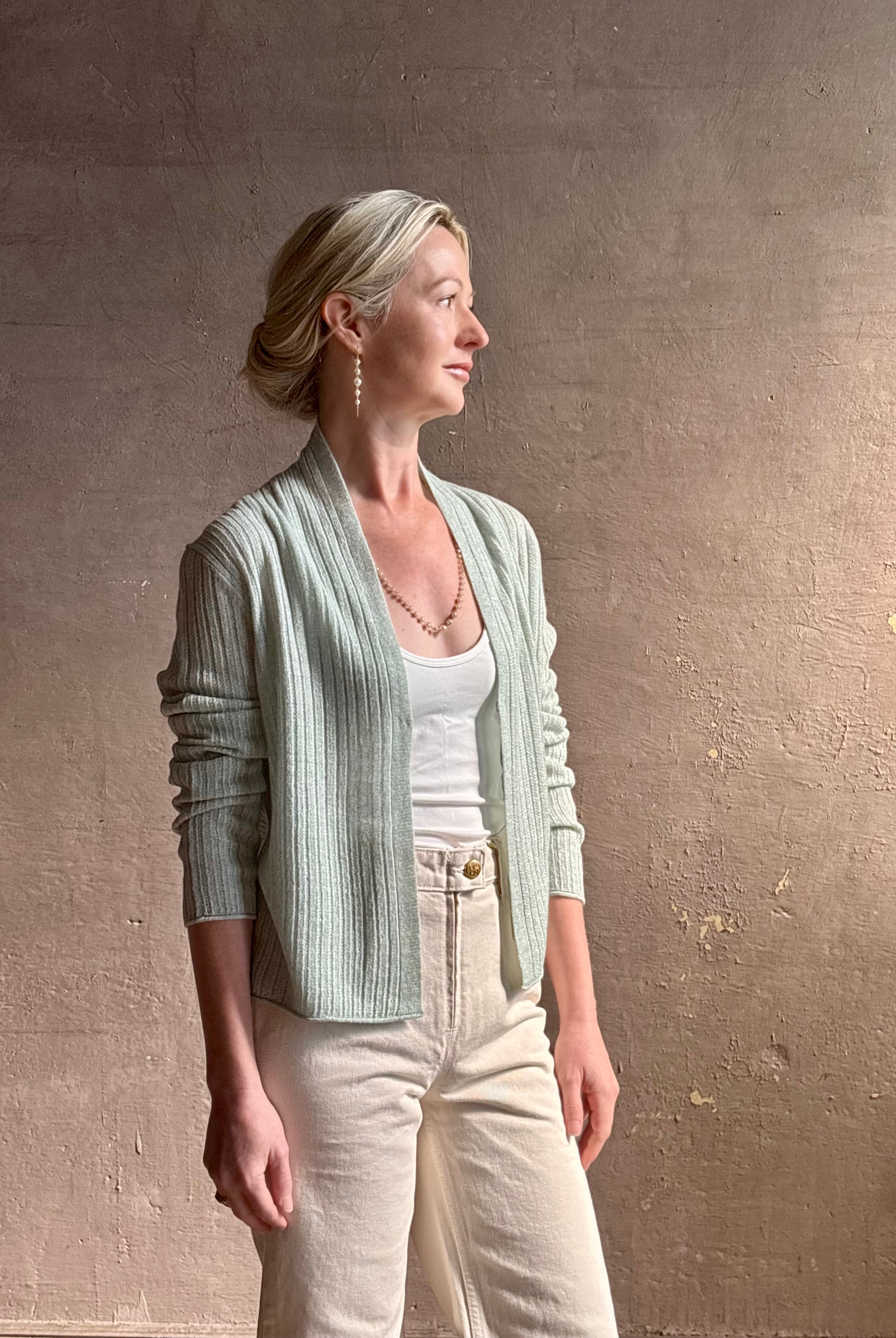 Mature woman wearing Rib Stealth Cardigan from Guest in Residence rendered in a serene sage brush aqua green and crafted from a refined blend of 58% cashmere and 42% linen with long sleeves and a hidden hook and eye closure