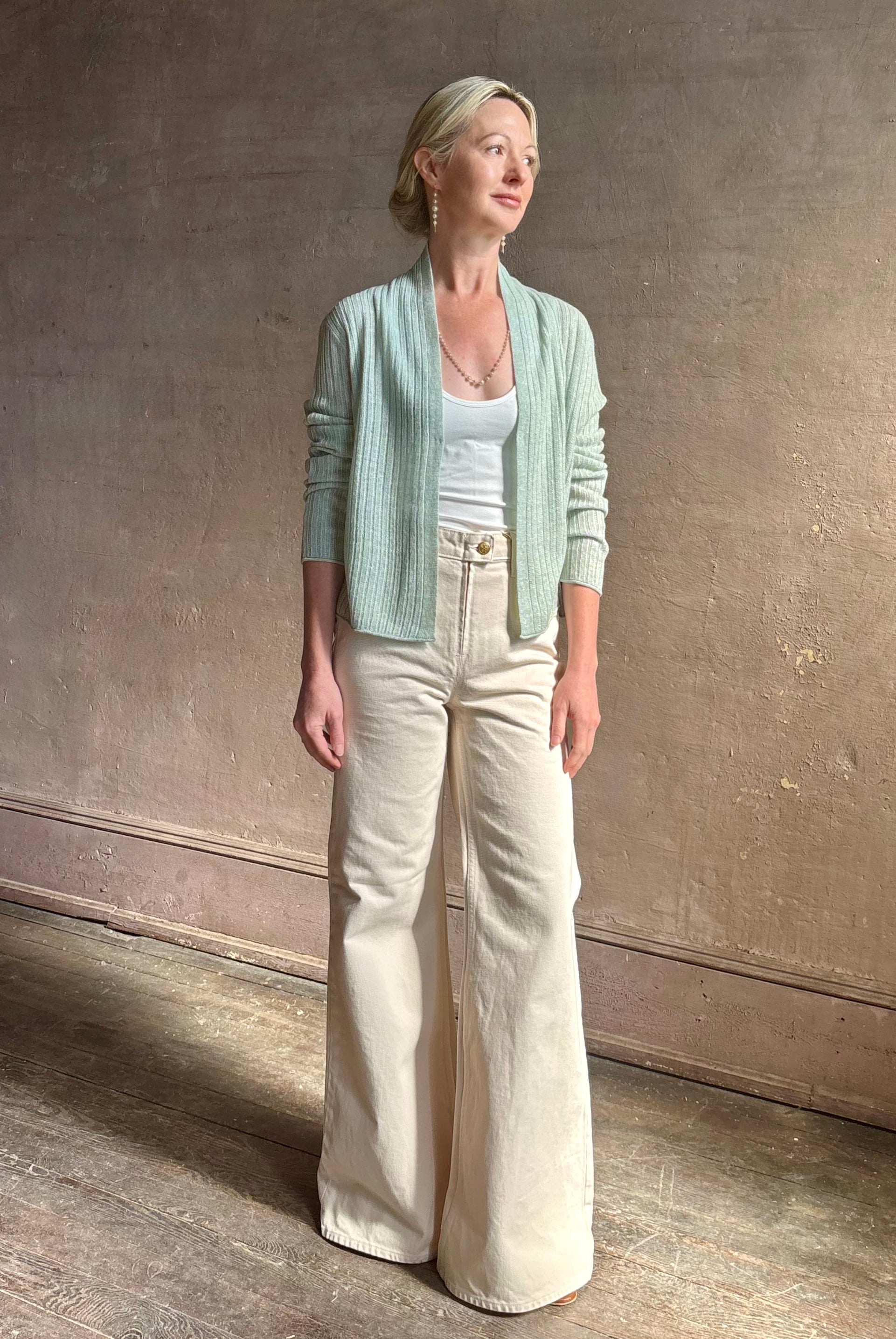 Mature woman wearing Rib Stealth Cardigan from Guest in Residence rendered in a serene sage brush aqua green and crafted from a refined blend of 58% cashmere and 42% linen with long sleeves and a hidden hook and eye closure