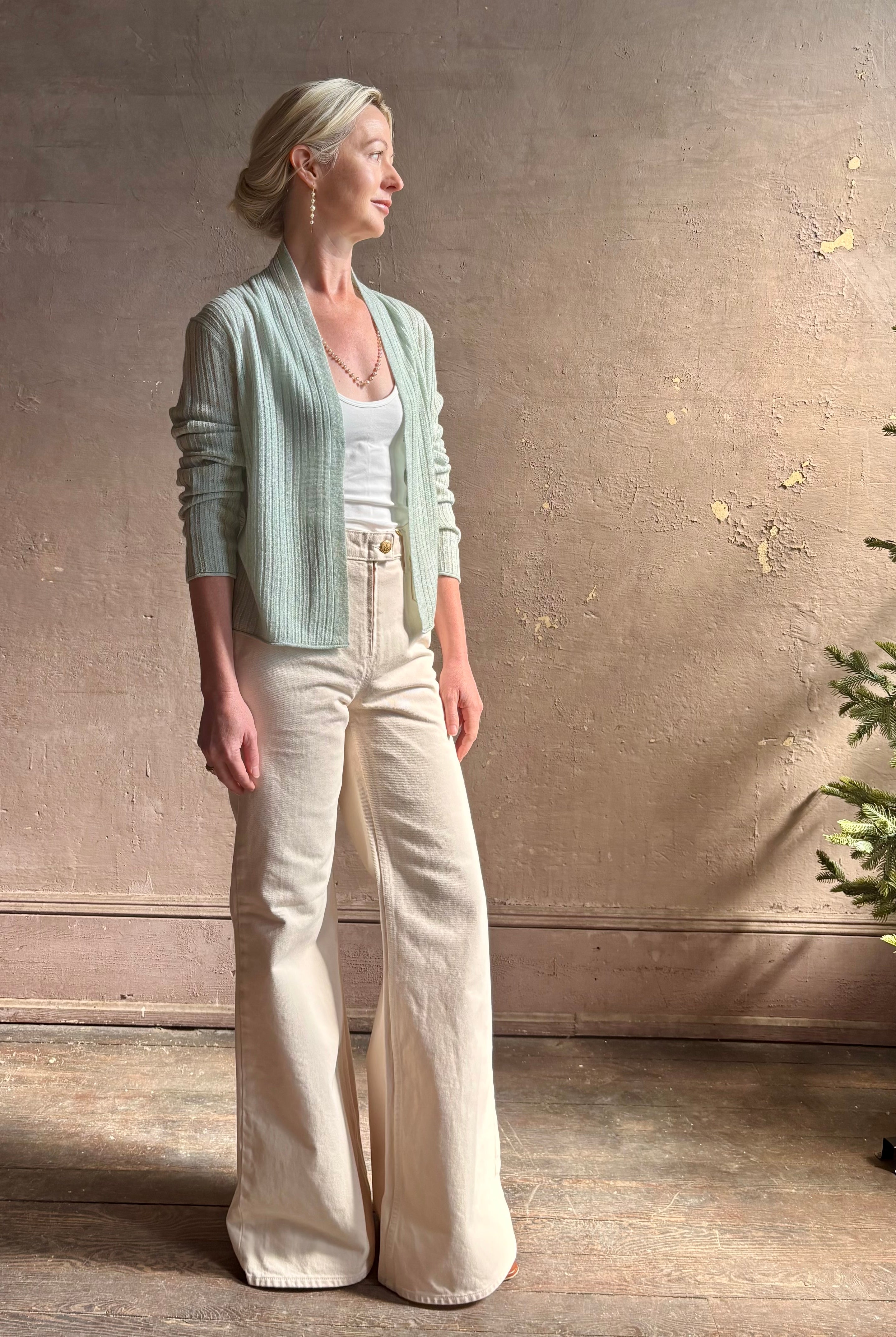 Mature woman wearing Rib Stealth Cardigan from Guest in Residence rendered in a serene sage brush aqua green and crafted from a refined blend of 58% cashmere and 42% linen with long sleeves and a hidden hook and eye closure
