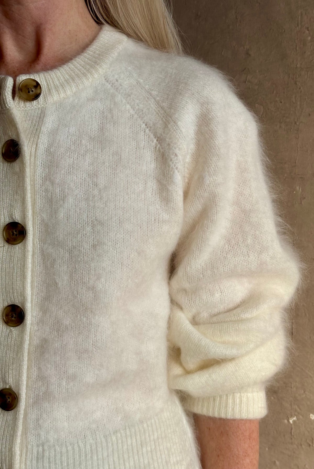 Close up image of Mature woman wearing Guest in Residence’s Grizzly Sculptured Cream brushed cashmere cardigan with henley style long sleeves and contrasting brown buttons