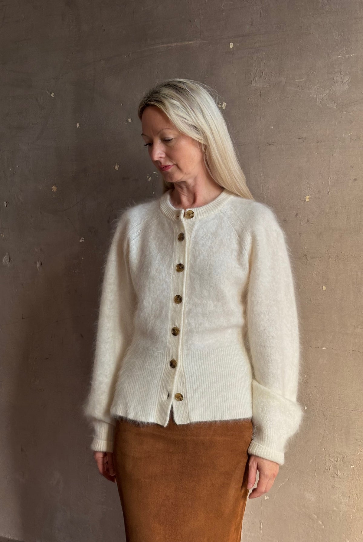 Mature woman wearing Guest in Residence’s Grizzly Sculptured Cream brushed cashmere cardigan ribbed trims brown buttons down front henley style long sleeves