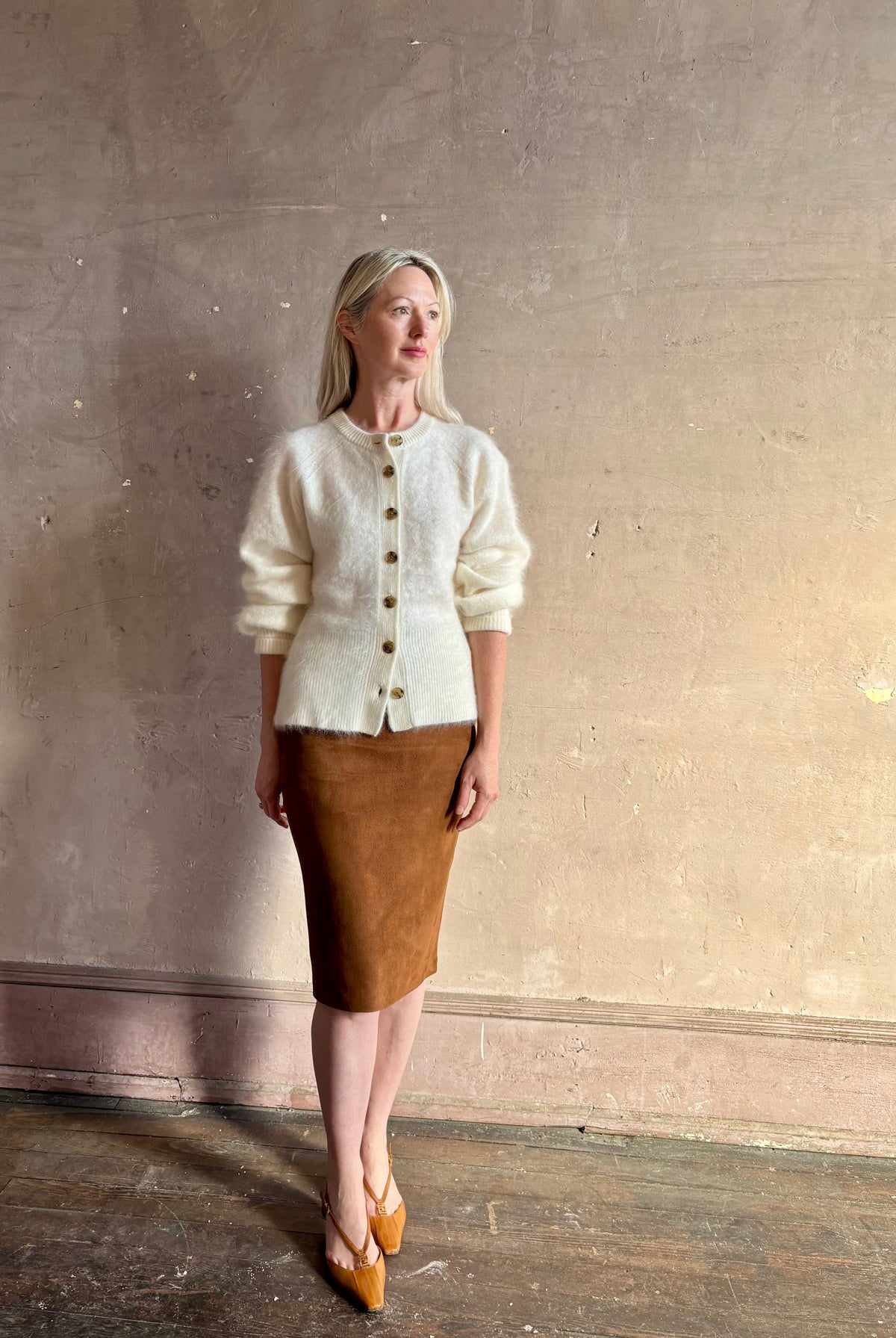 Mature woman wearing a cream-colored brushed cashmere cardigan with brown buttons by Gigi Hadid Guest in Residence suede leather skirt and Fendi Shoes
