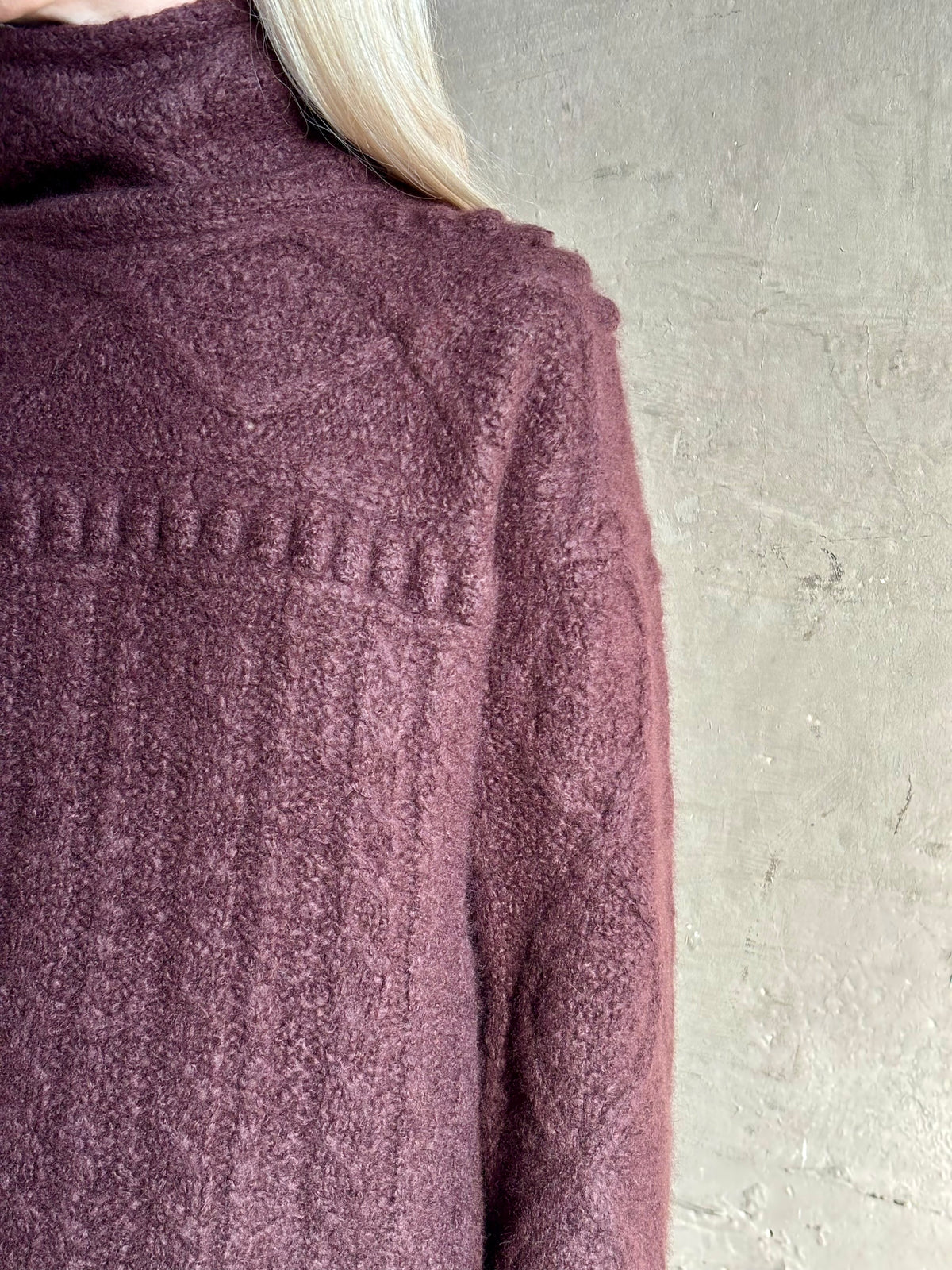 Close-up of a woman wearing a textured cable knit turtleneck sweater in a fig purple Guest in Residence Super Cloud T Neck cashmere-silk cloud-soft warmth