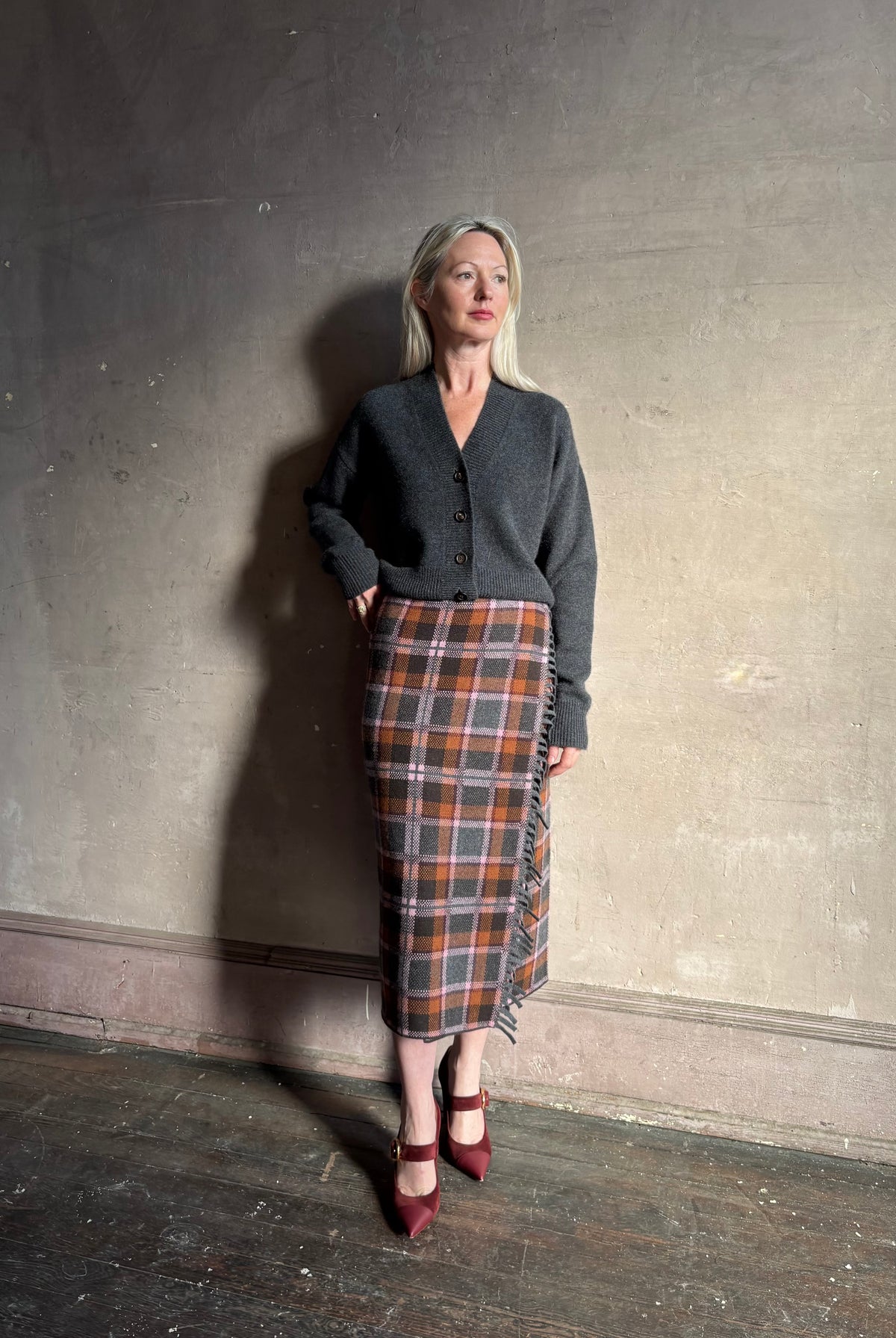 Mature woman wearing a dark gray brown and orange plaid wrap pencil skirt trimmed with fringe by Guest in Residence