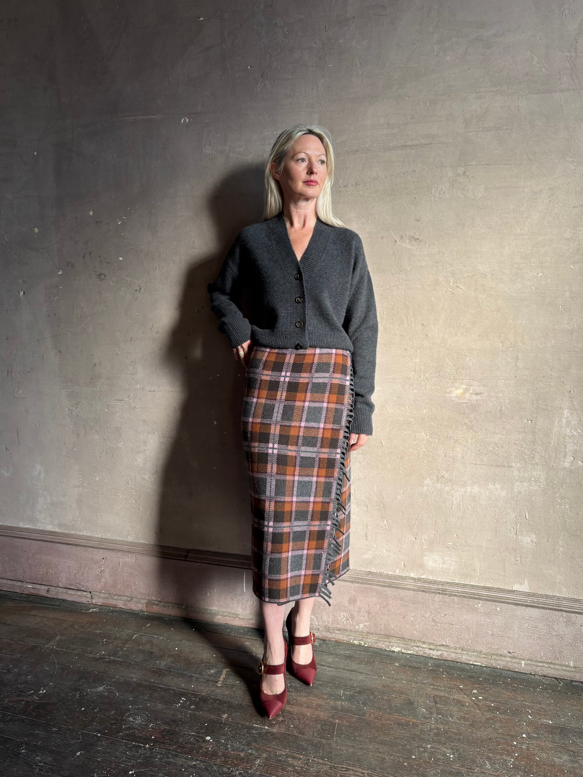 Mature woman wearing a dark gray brown and orange plaid wrap pencil skirt trimmed with fringe by Guest in Residence