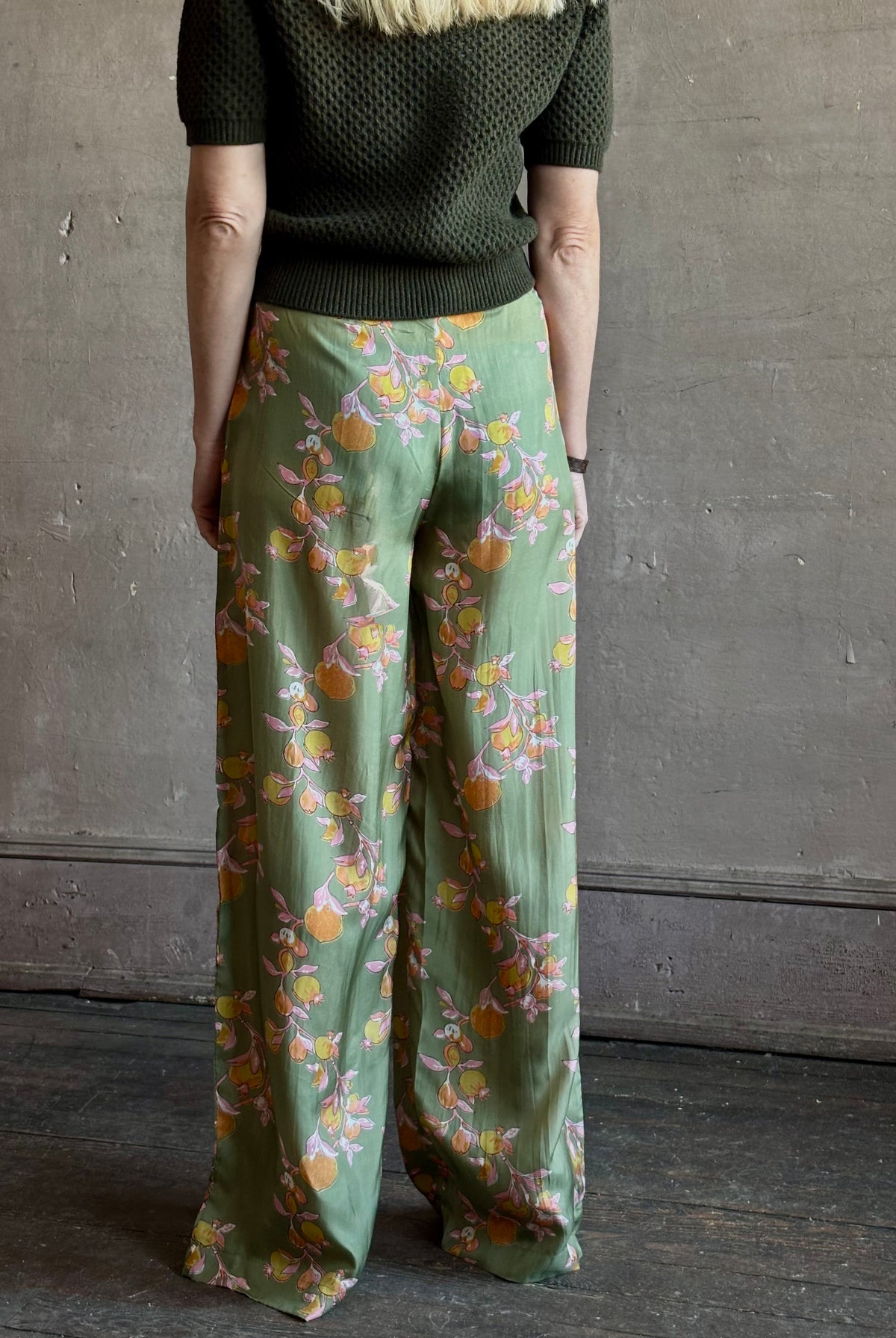 Mature woman wearing Hannah Artwear Azra silk Pant Khaki habotai with vibrant pomegranate print relaxed straight leg Fluid artisan-printed