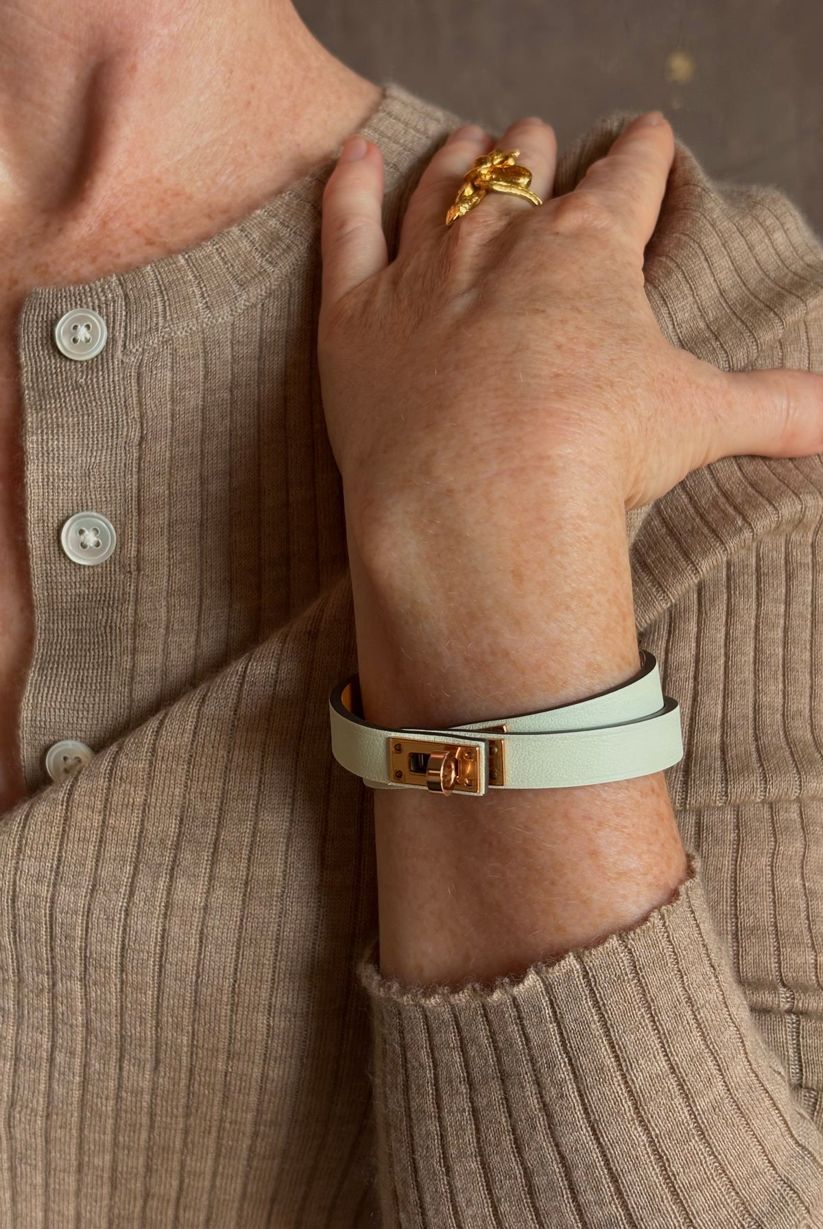 Mature woman wearing Hermès' Mini Kelly Double Tour Wrap Bracelet in Vert d'Eau & Rose Gold pristine, never-worn leather with the iconic Kelly turn-lock. Rare, collectible French luxury