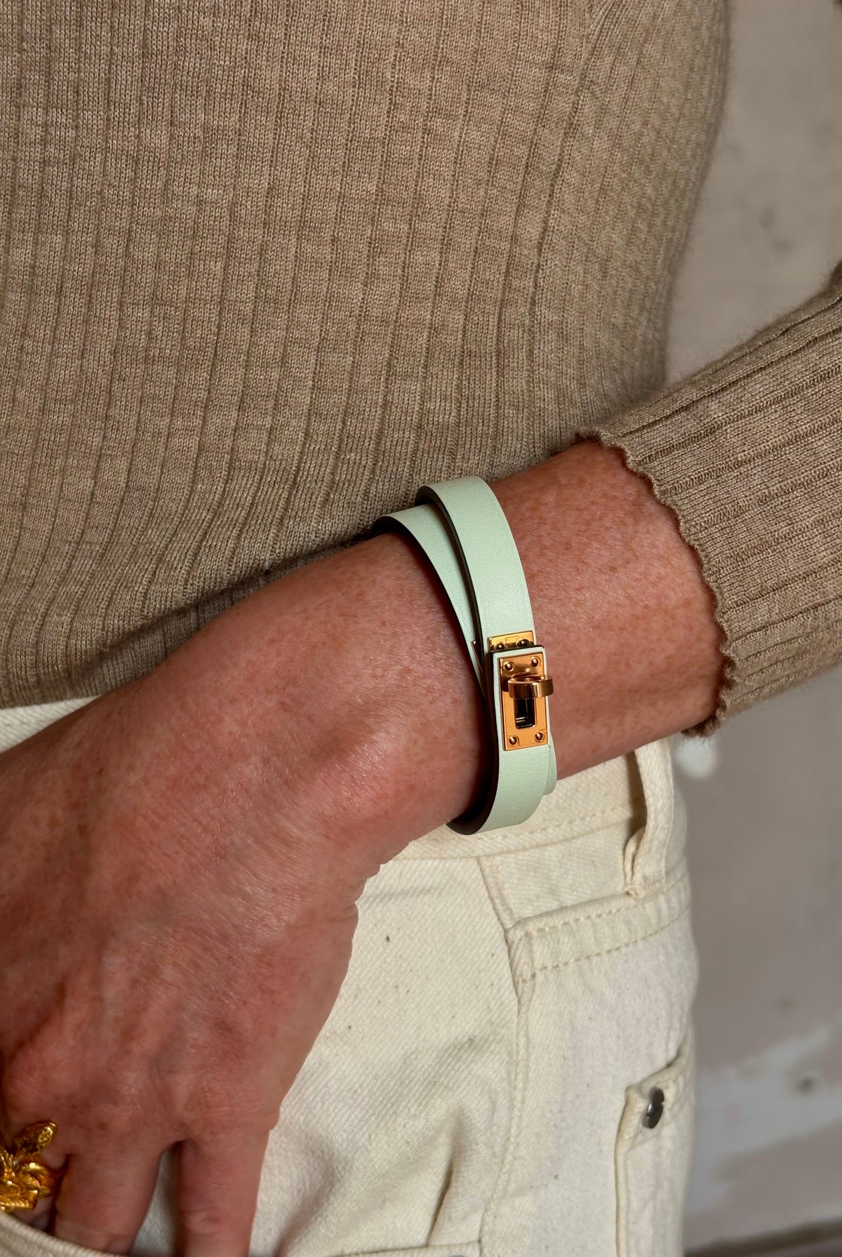 Mature woman wearing Hermès' Mini Kelly Double Tour Wrap Bracelet in Vert d'Eau & Rose Gold pristine, never-worn leather with the iconic Kelly turn-lock. Rare, collectible French luxury