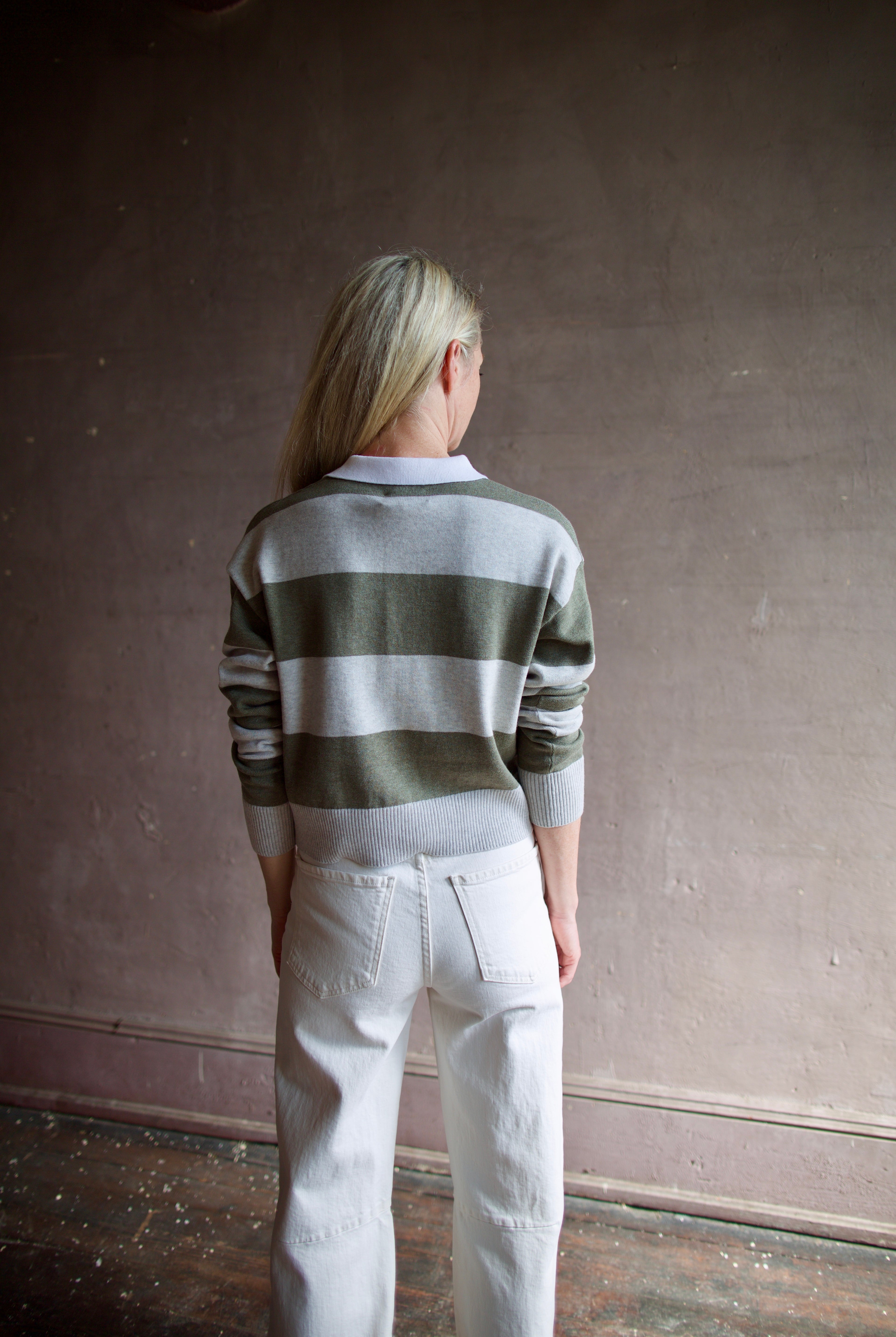 Model wearing Le Jean long sleeve polo in cotton and cashmere featuring a large green and gray stripe with a white collar.