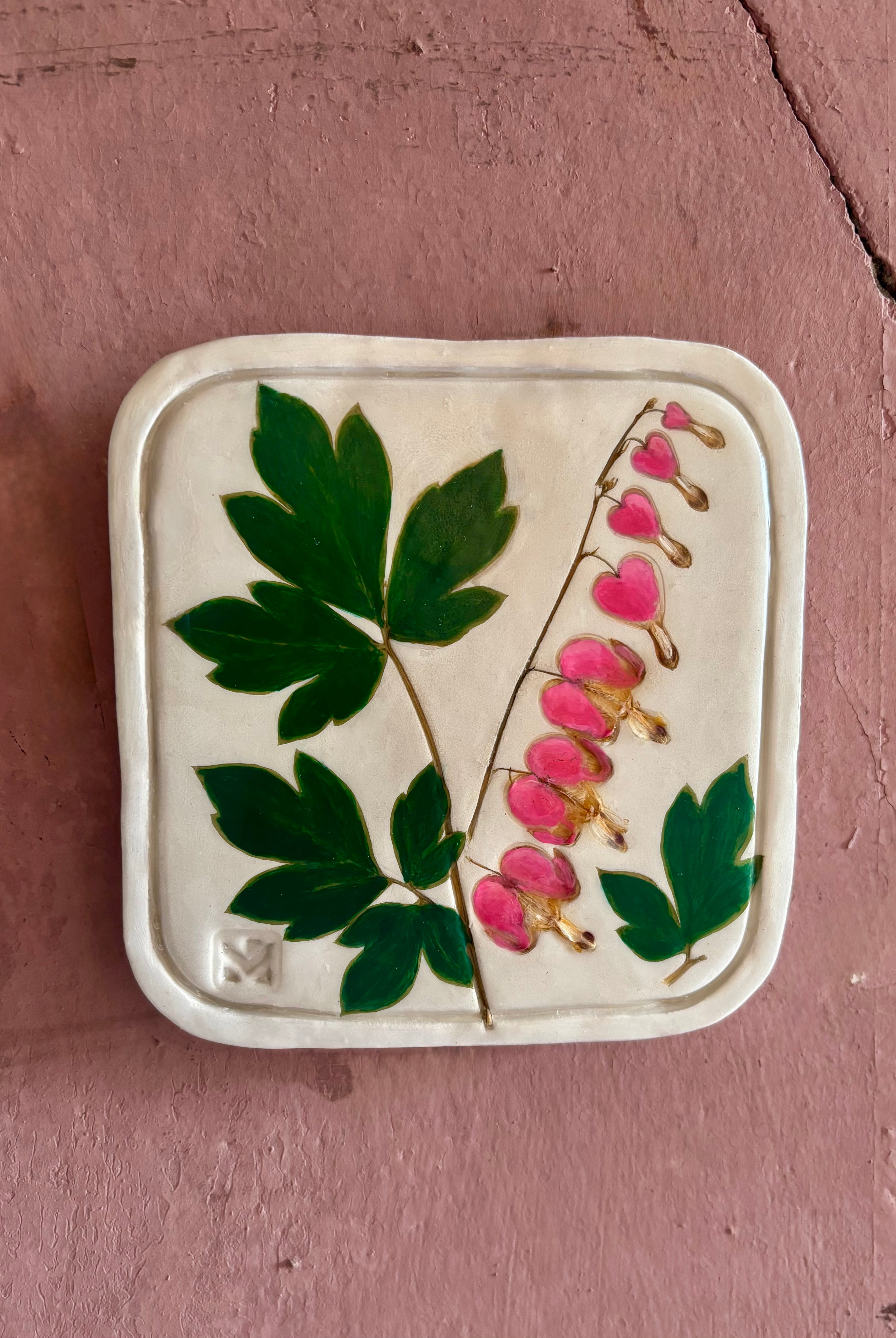 A square ceramic tile with botanical pressed bleeding heart flower stem and foliage on cream clay by NC artist