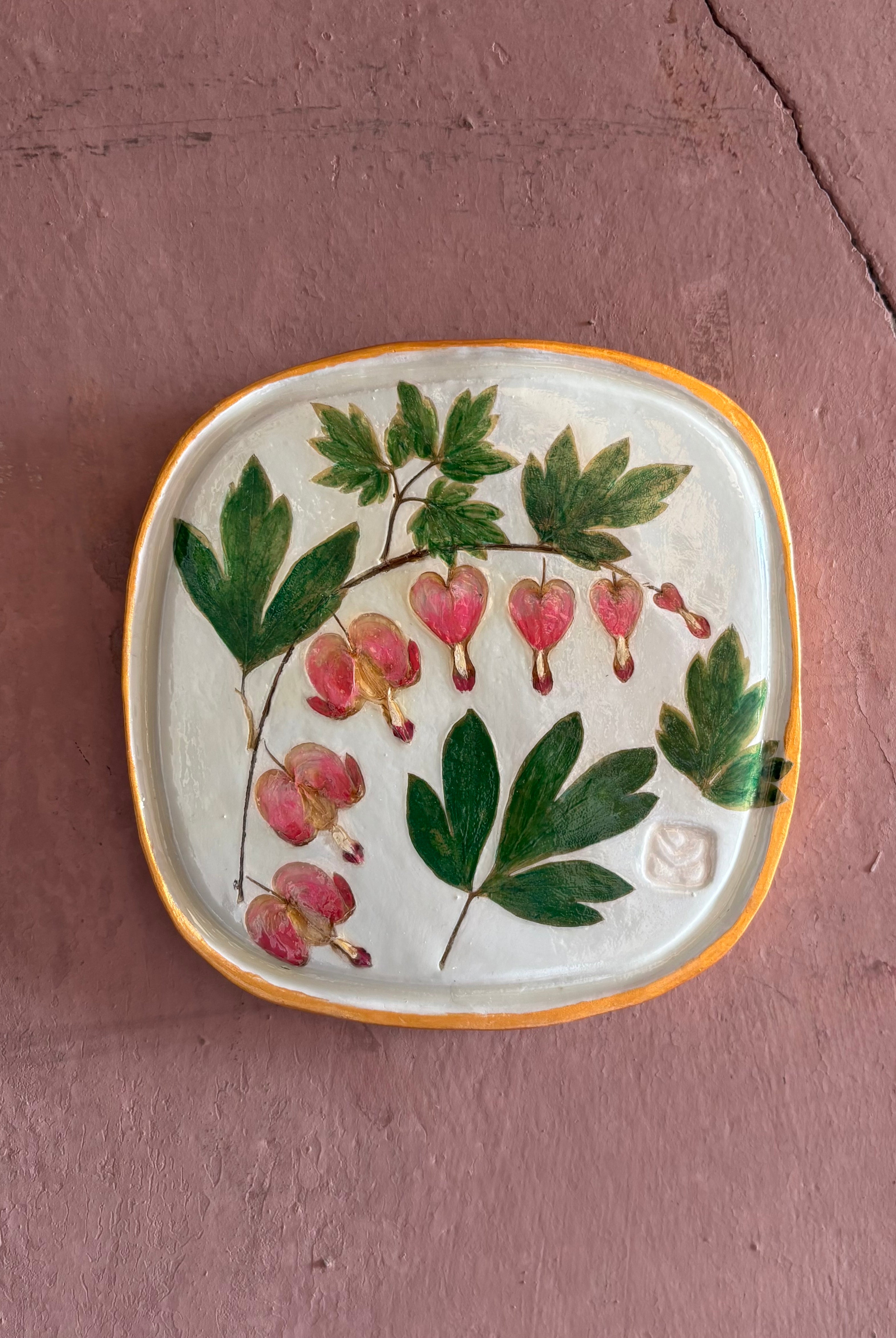 A square ceramic tile with botanical pressed bleeding heart flower stem and foliage on cream clay by NC artist