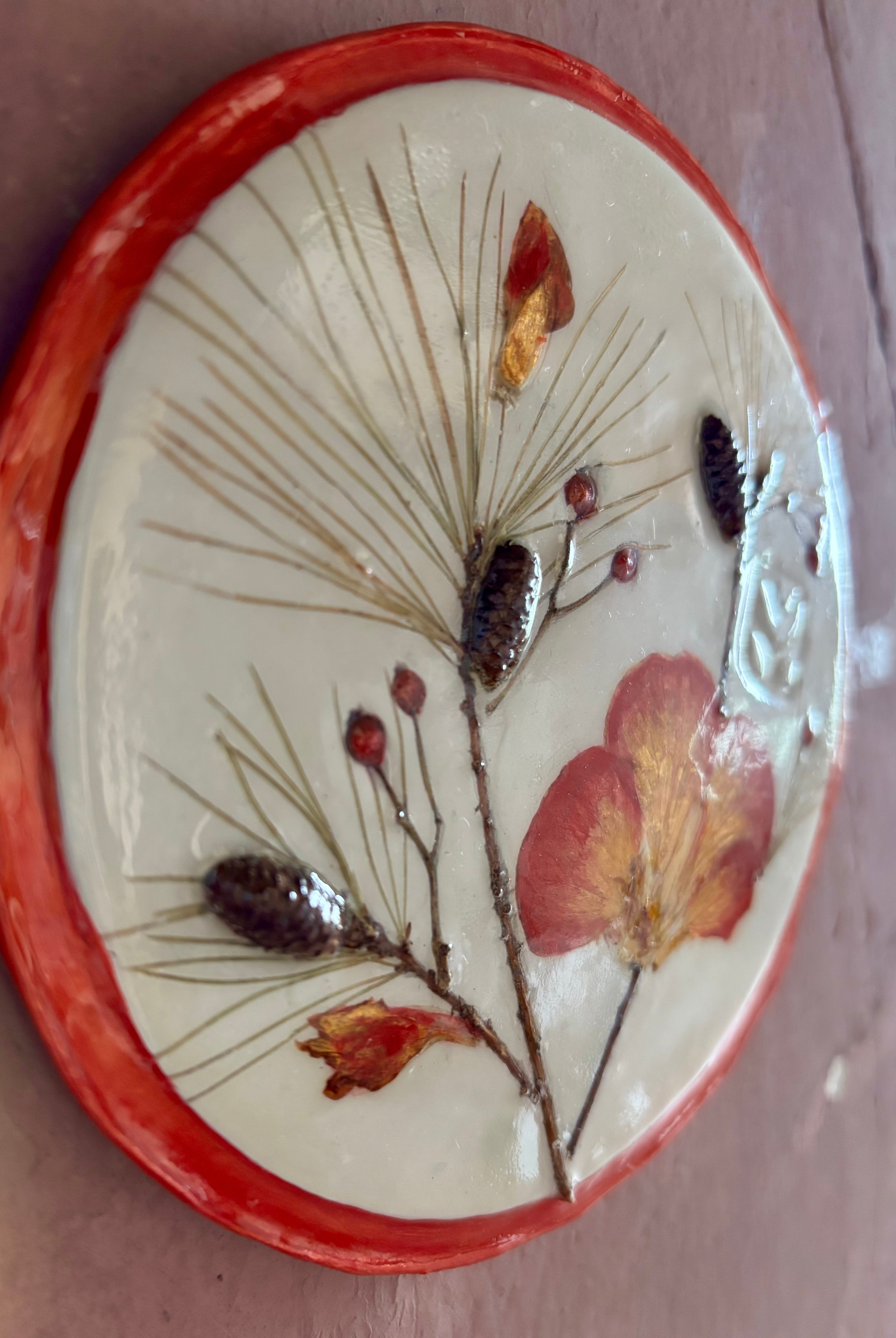 A round ceramic wall plaque pressed botanical elements holly azalea pine needles pinecones and red berries