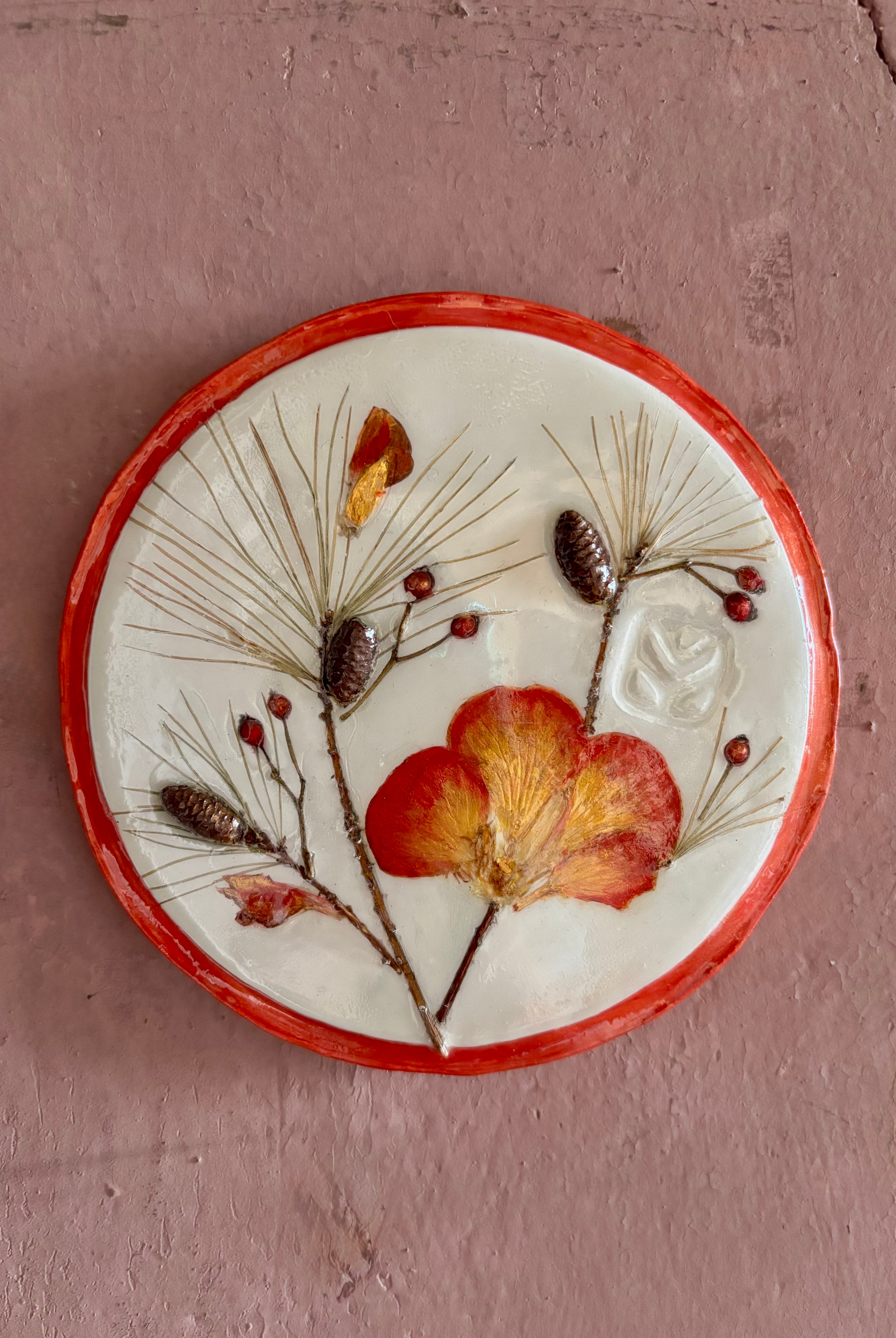 A round ceramic wall plaque pressed botanical elements holly azalea pine needles pinecones and red berries
