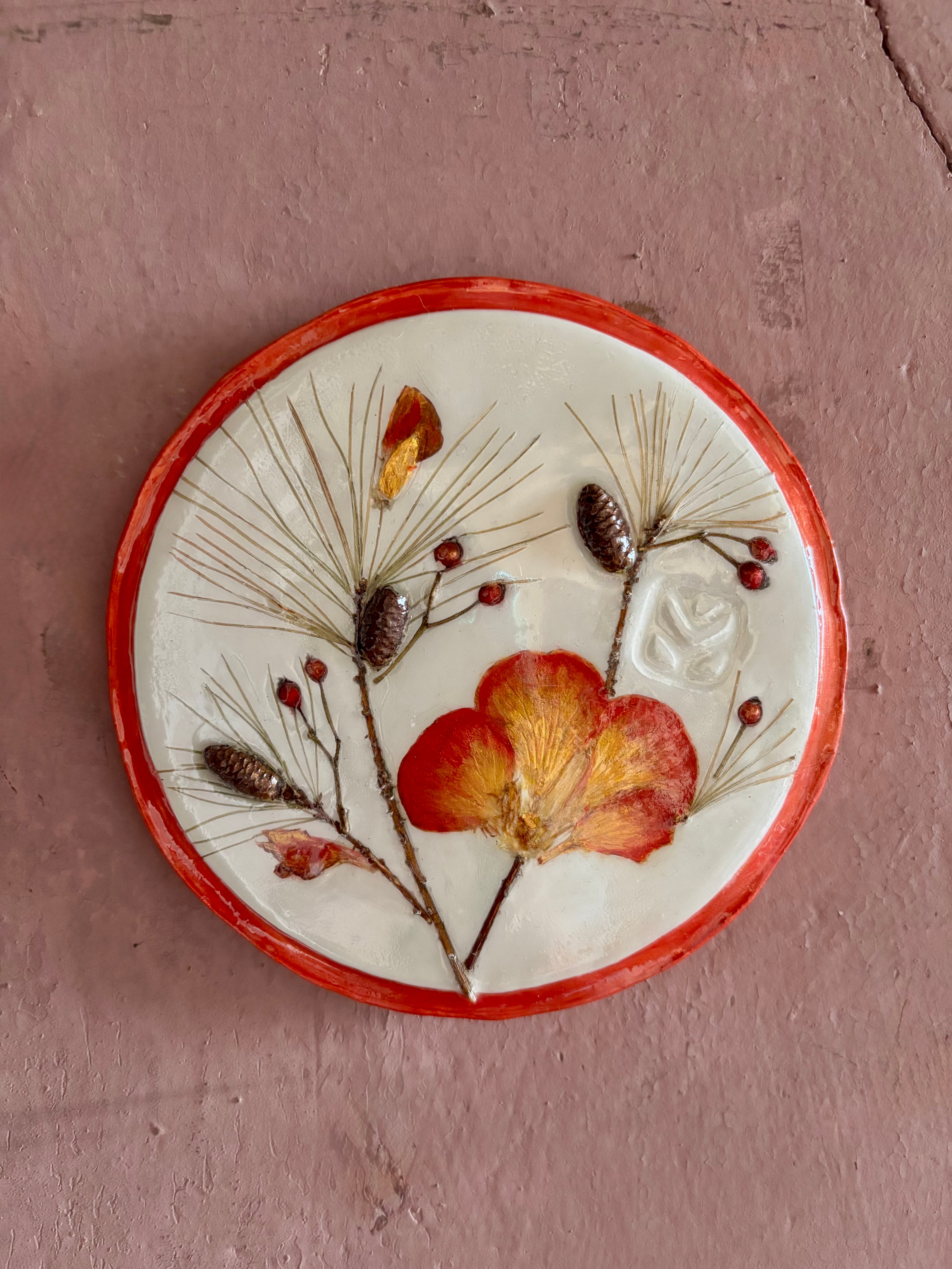 A round ceramic wall plaque pressed botanical elements holly azalea pine needles pinecones and red berries