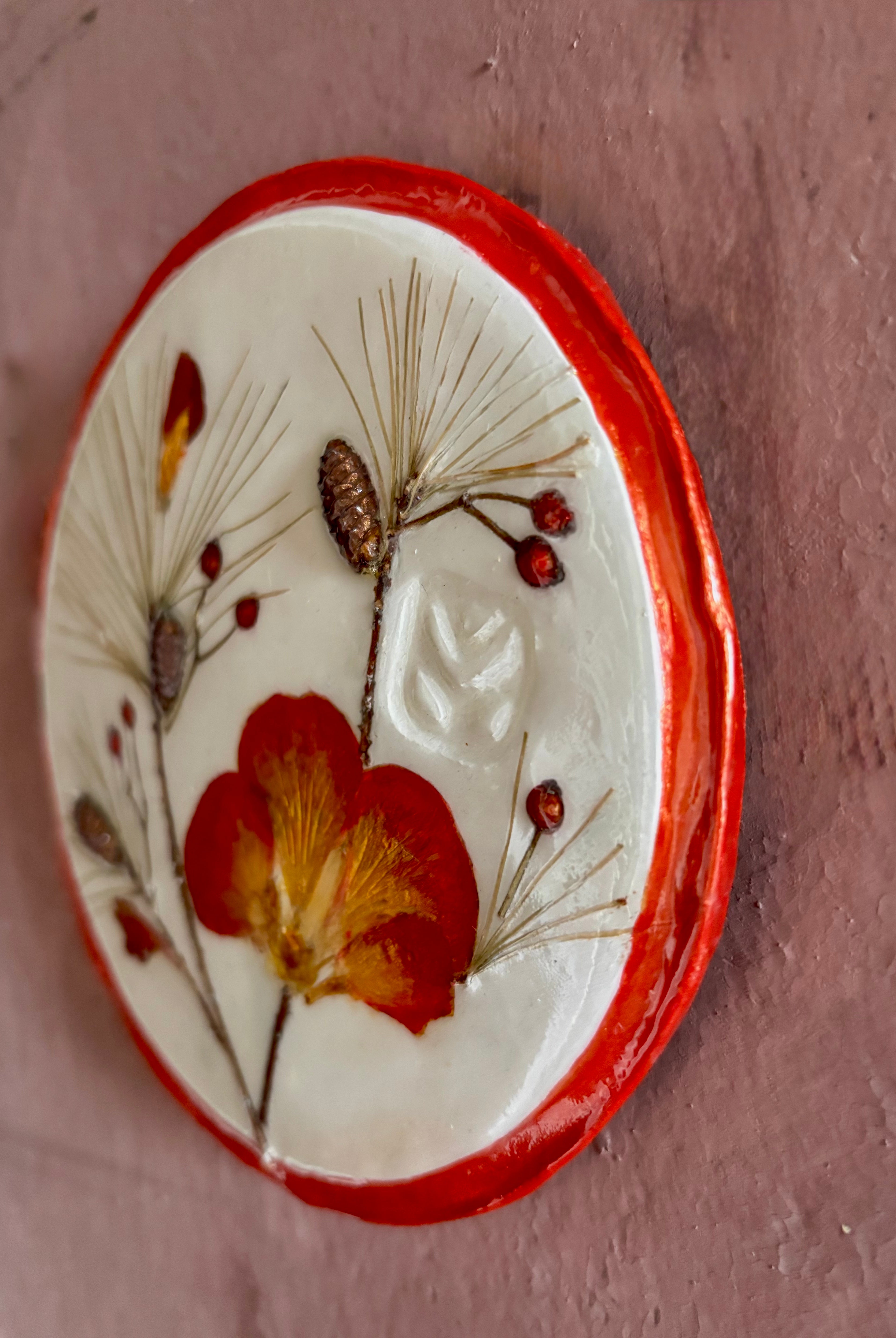 A round ceramic wall plaque pressed botanical elements holly azalea pine needles pinecones and red berries