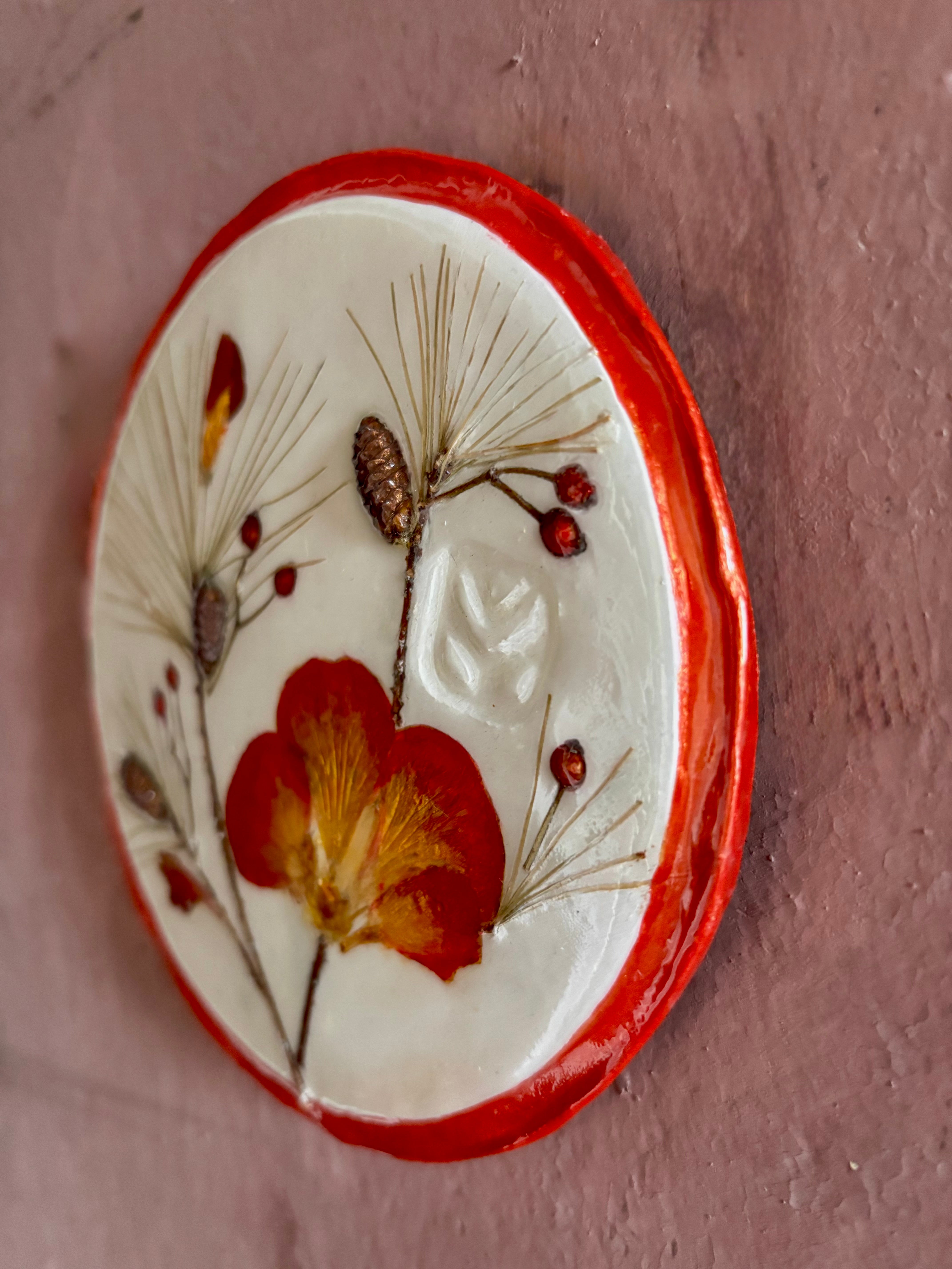 A round ceramic wall plaque pressed botanical elements holly azalea pine needles pinecones and red berries