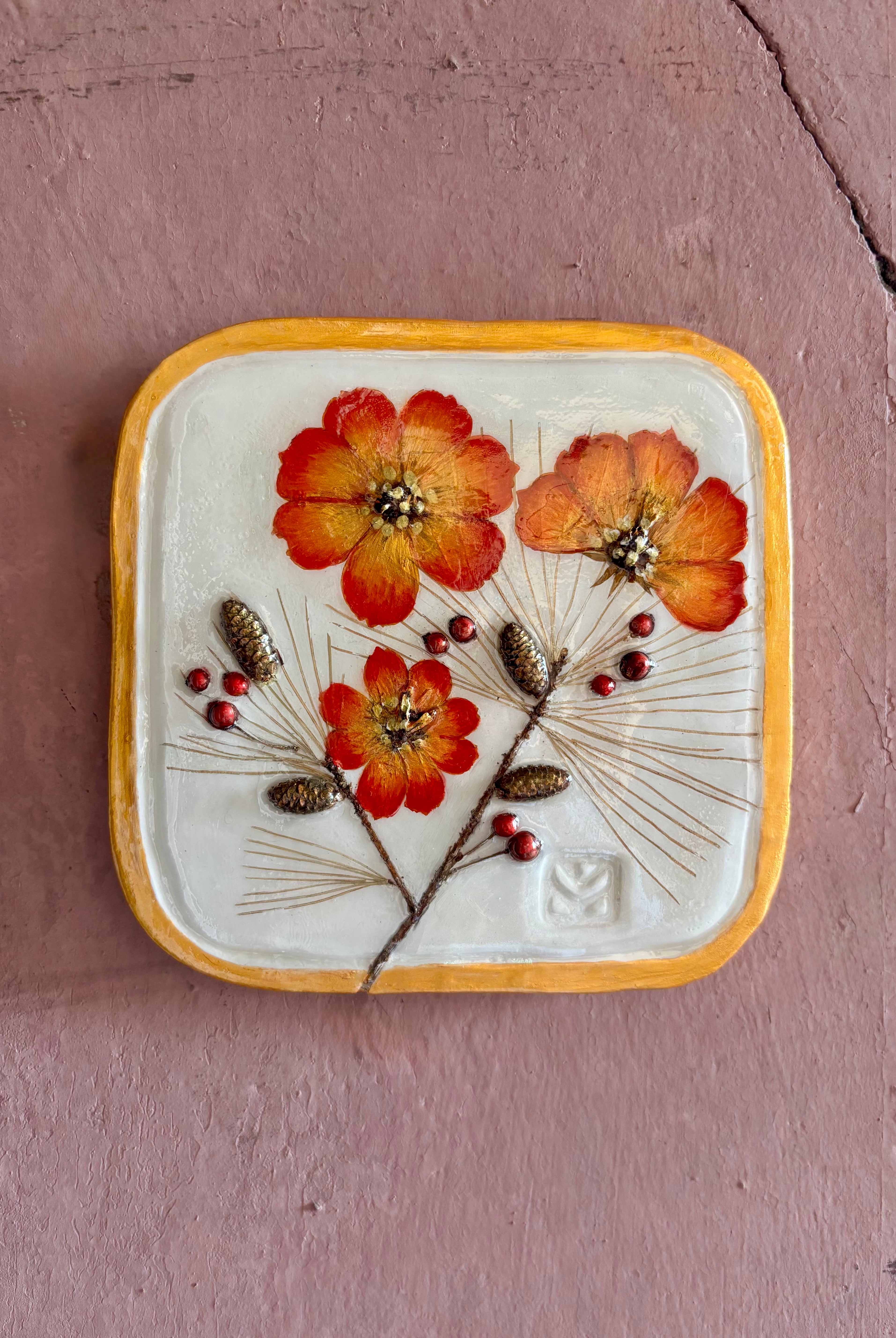 A square ceramic wall plaque pressed botanical elements holly cosmos pine needles pinecones and red berries