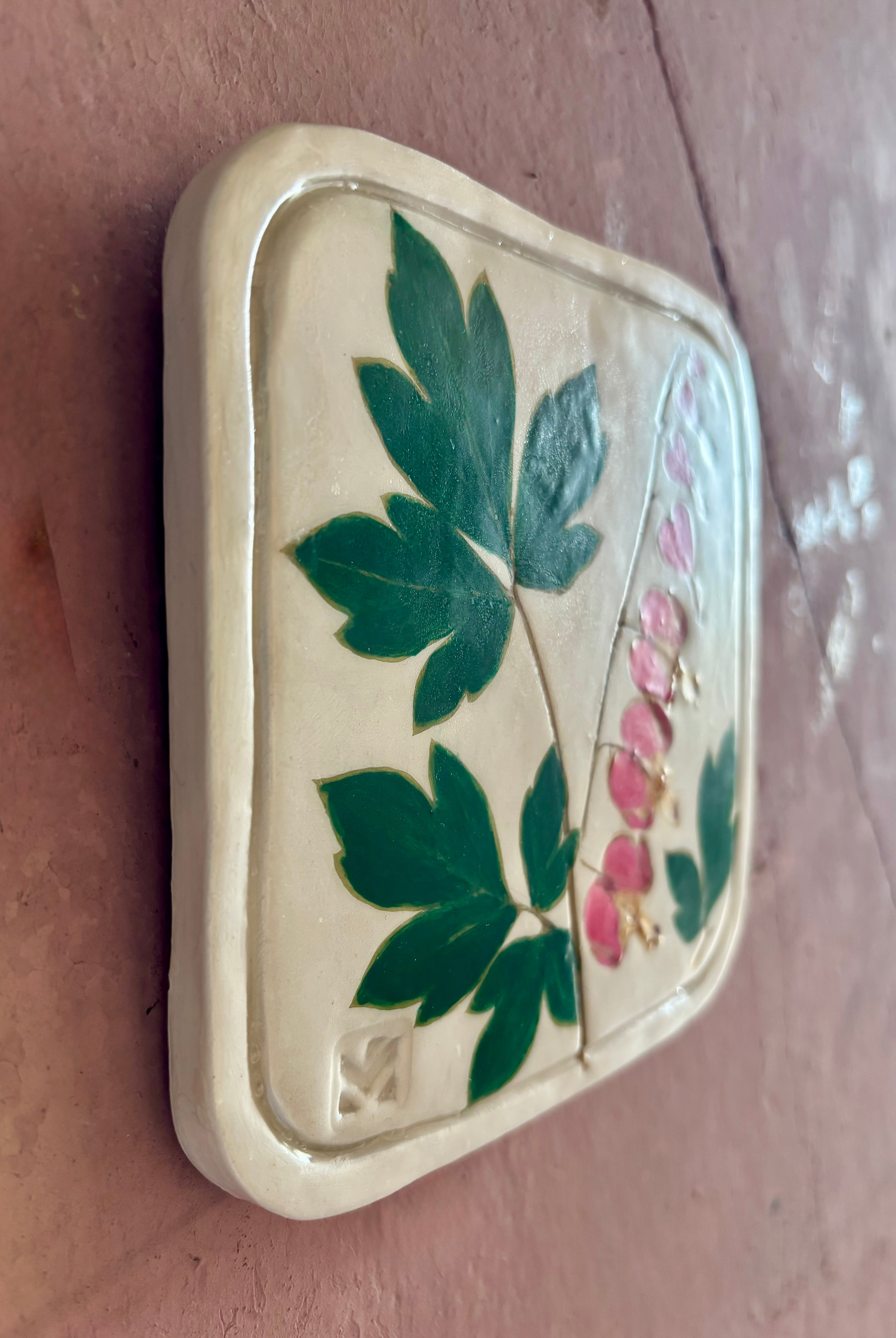 A square ceramic tile with botanical pressed bleeding heart flower stem and foliage on cream clay by NC artist