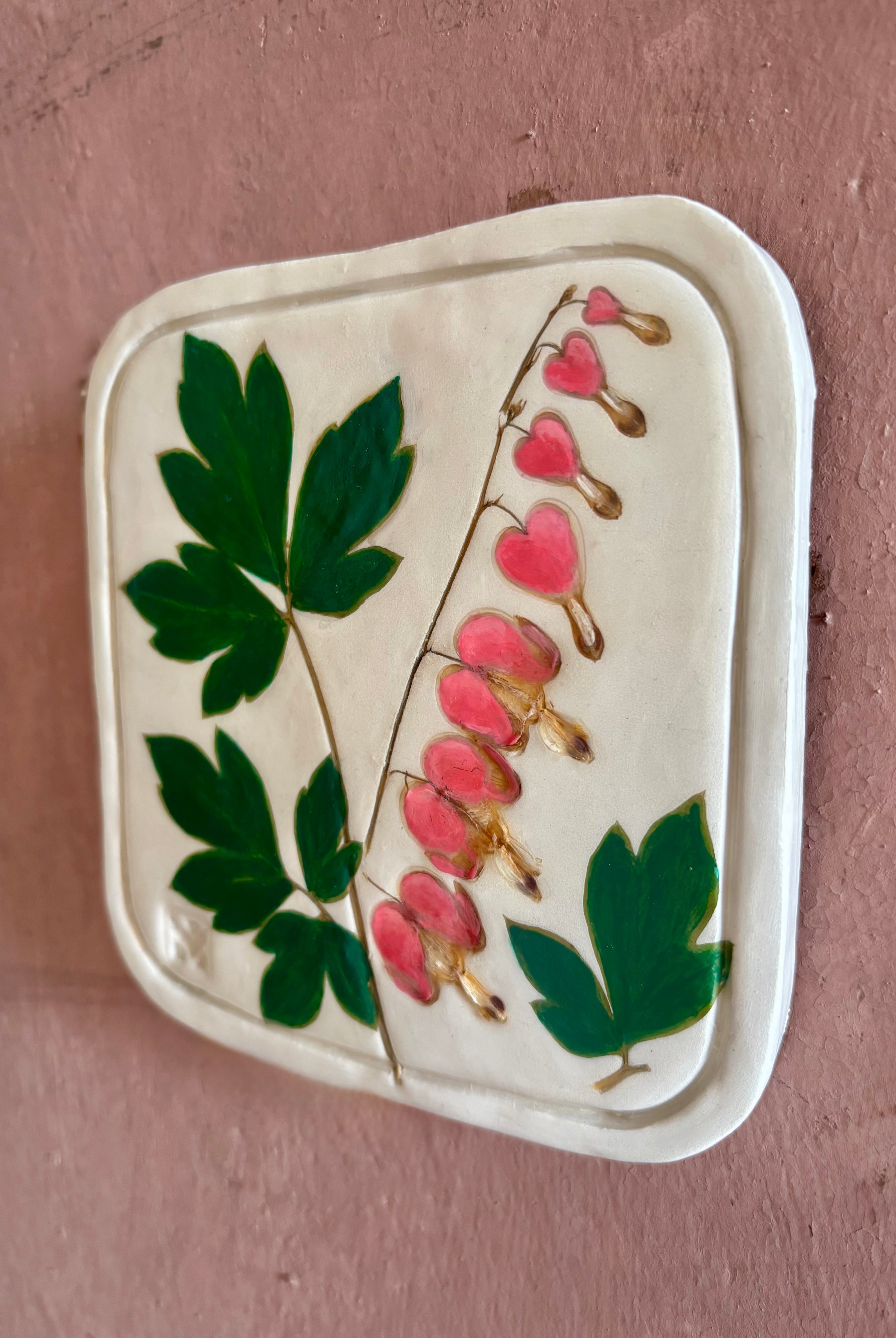 A square ceramic tile with botanical pressed bleeding heart flower stem and foliage on cream clay by NC artist