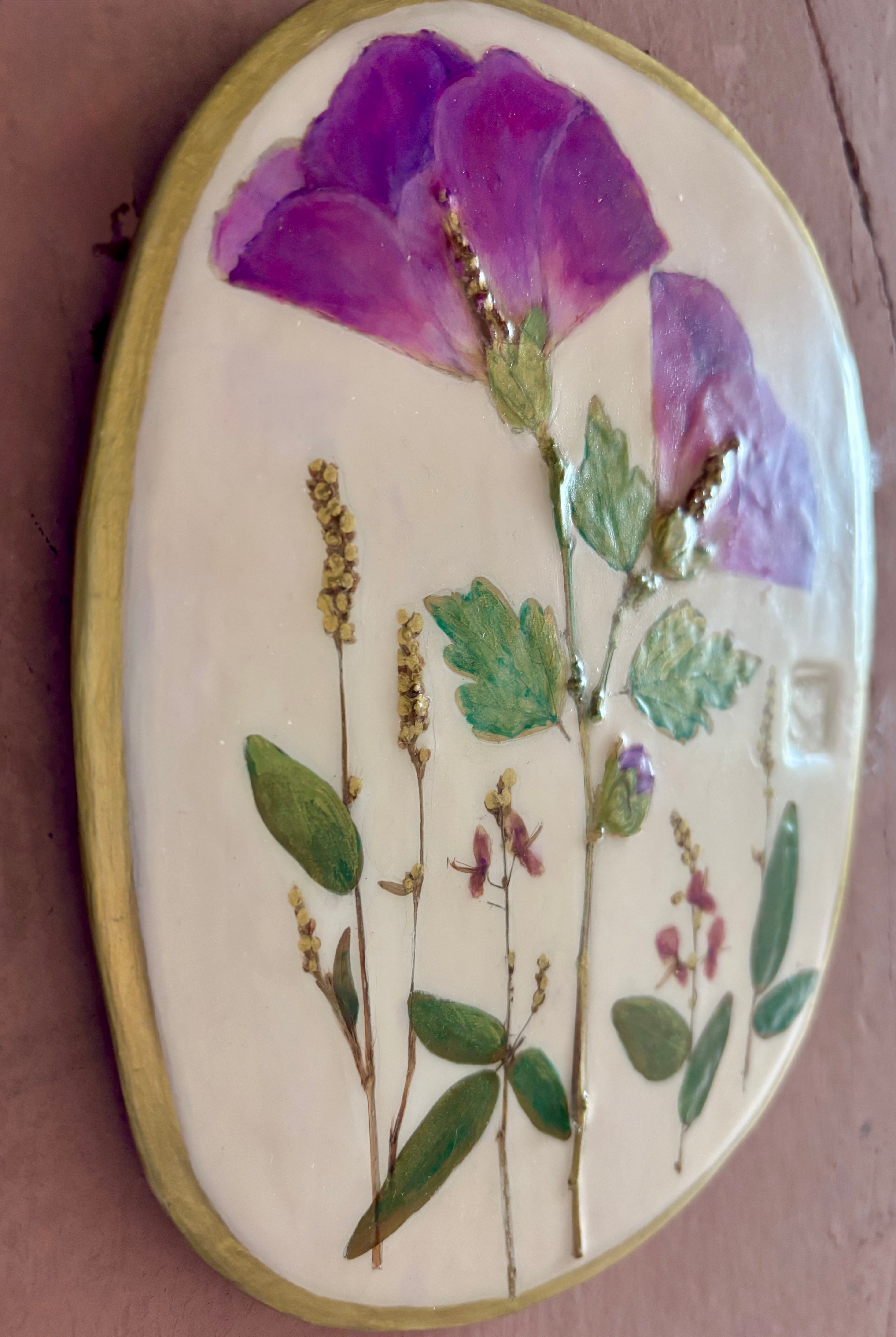An oval ceramic wall plaque featuring pressed purple rose of sharon hibiscus flowers and green leaves on white clay
