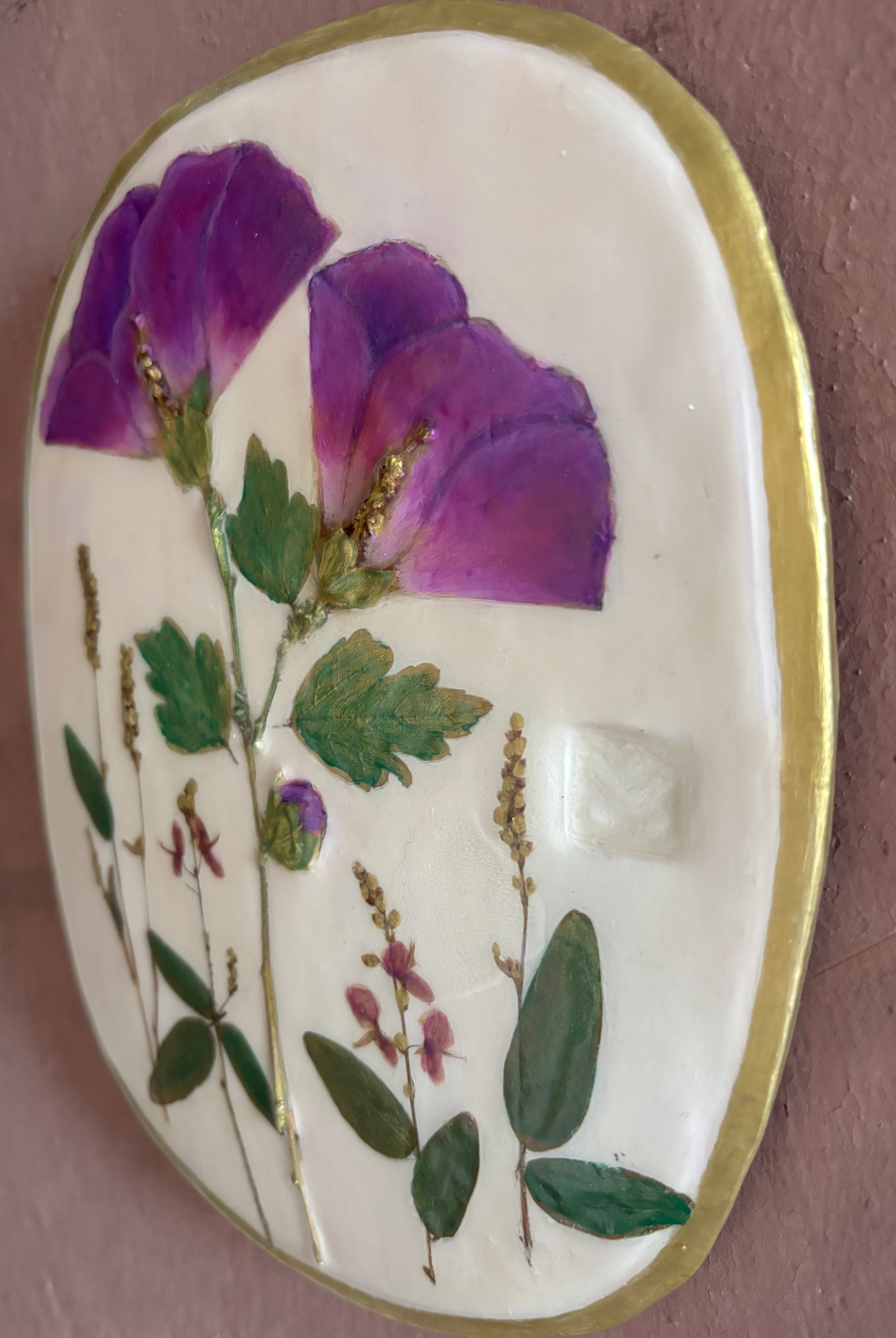 An oval ceramic wall plaque featuring pressed purple rose of sharon hibiscus flowers and green leaves on white clay
