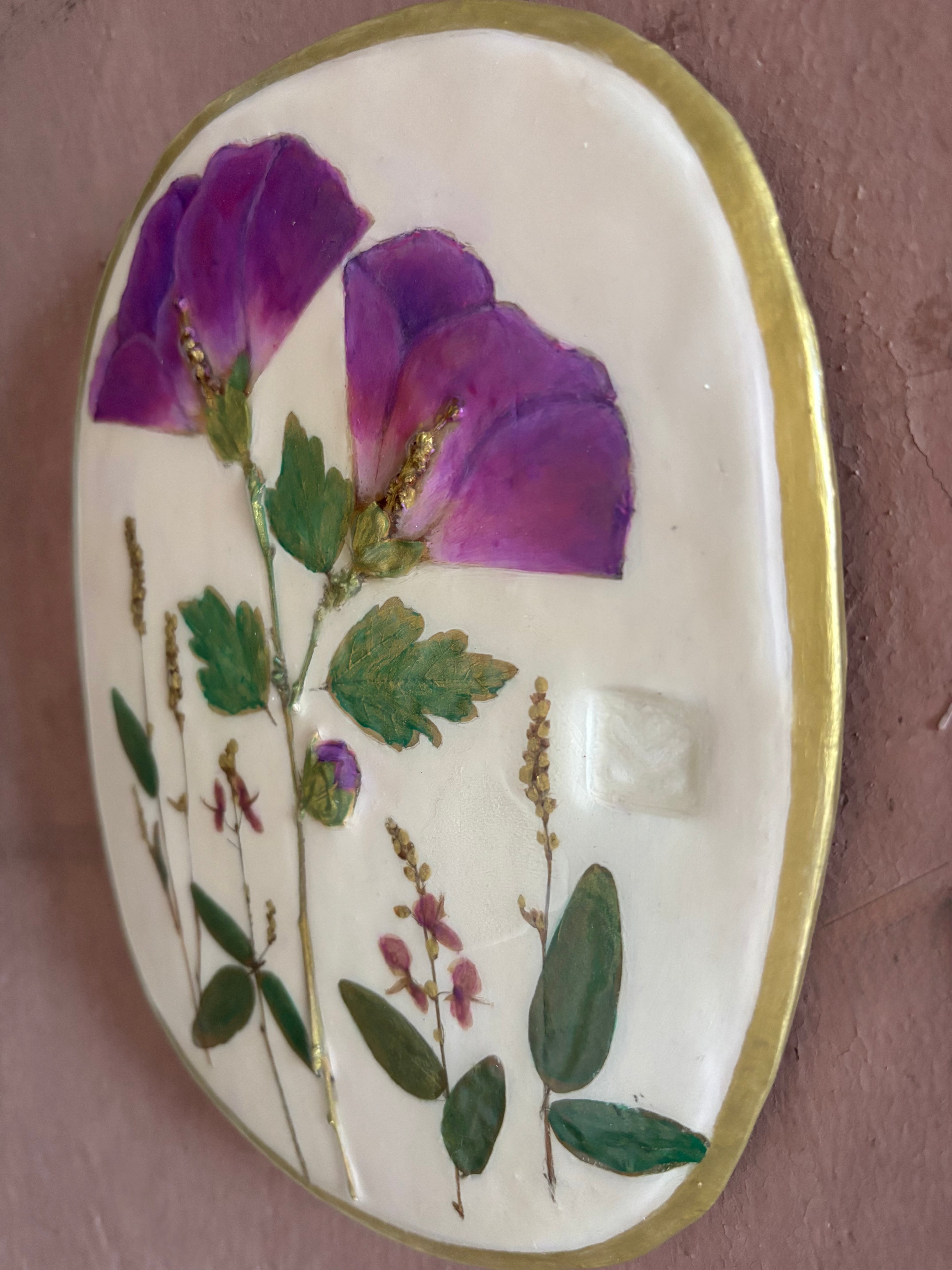 An oval ceramic wall plaque featuring pressed purple rose of sharon hibiscus flowers and green leaves on white clay