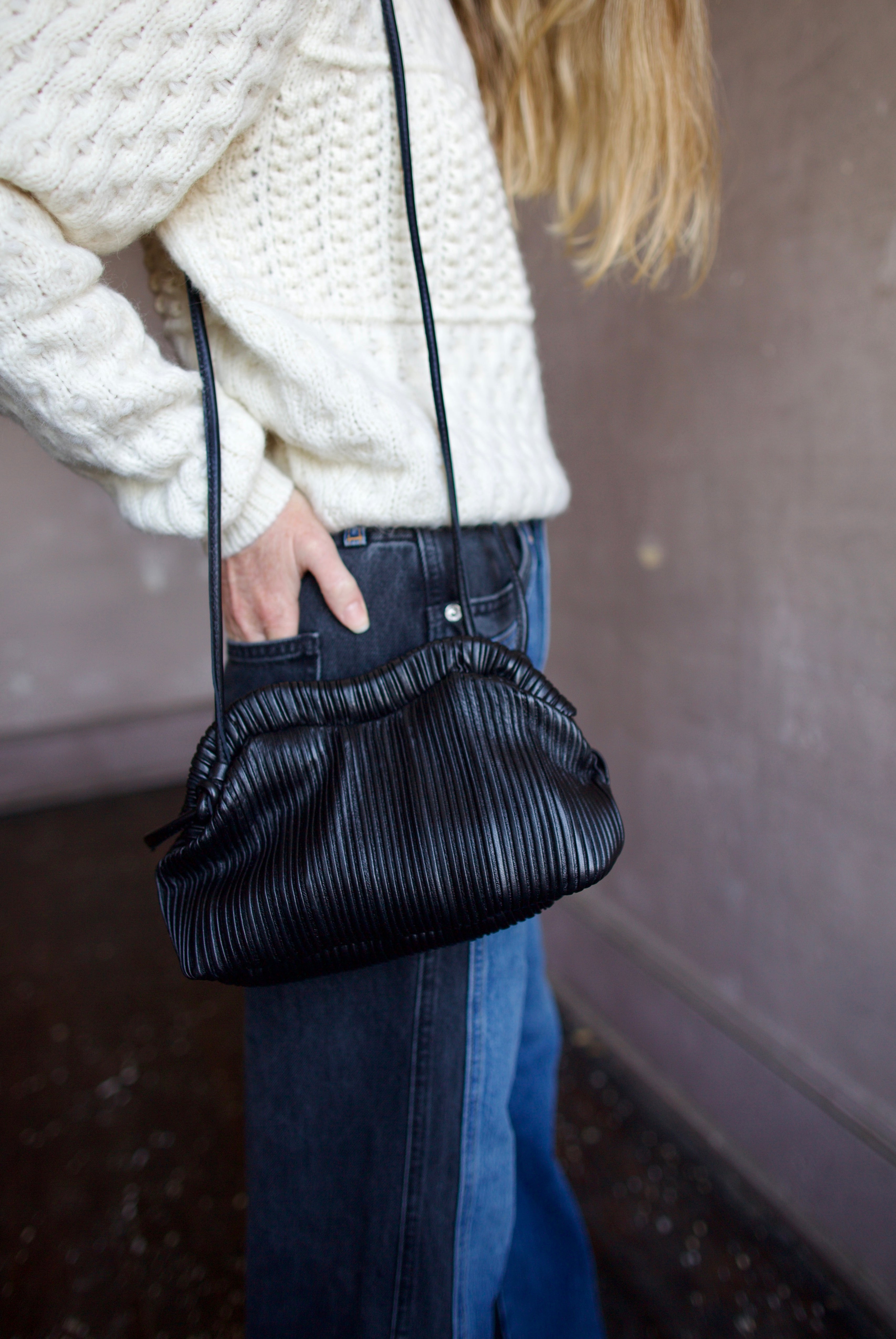 Image featuring a woman wearing the Baci handbag by Mansur Gavriel in black with a magnetic closure, adjustable crossbody strap and intricate pintucked leather across entire hand bag.