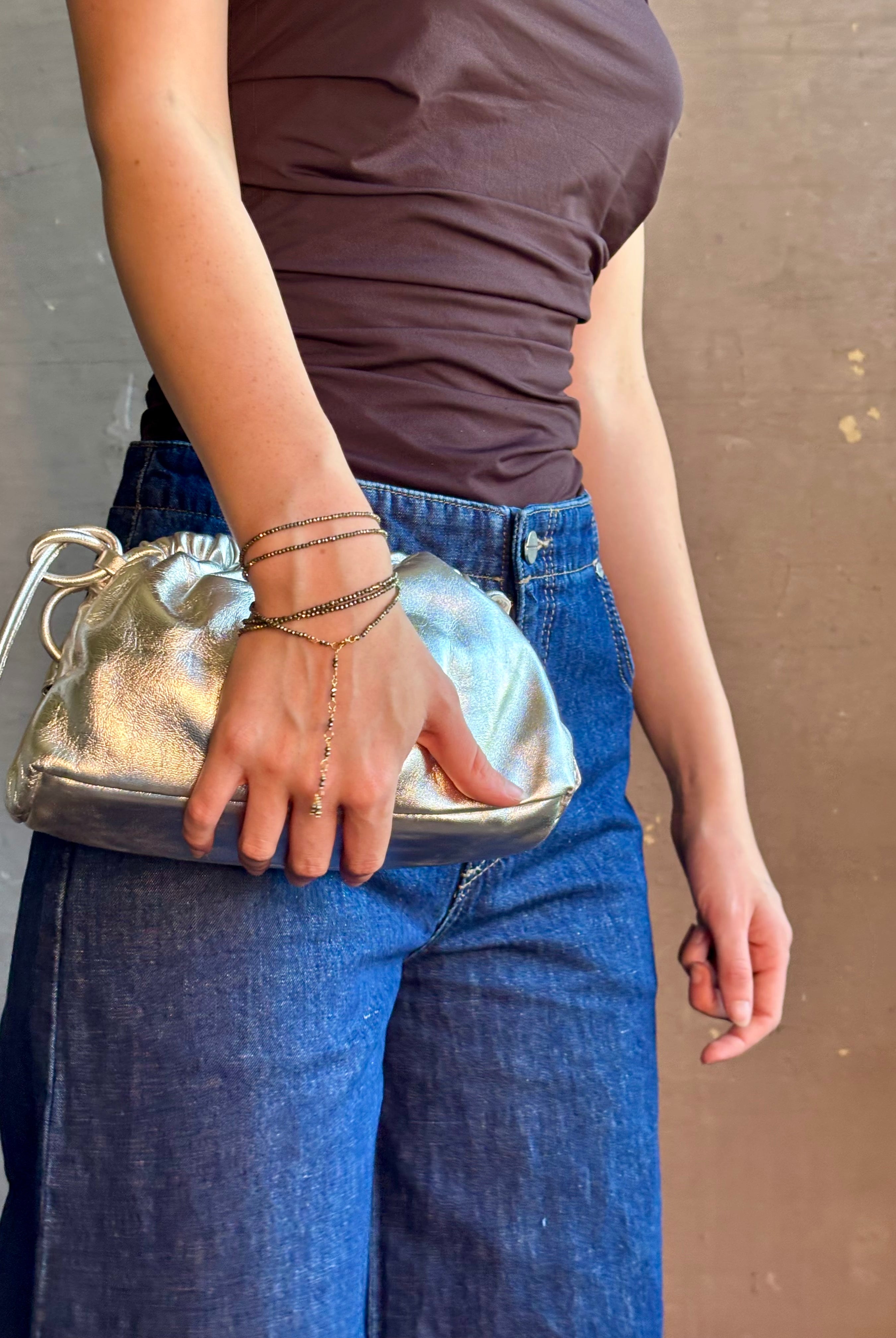 Woman wearing the Italian leather Mini Cloud crossbody by high-end designer Mansur Gavriel in metallic silver with removeable shoulder strap that can also double as a clutch