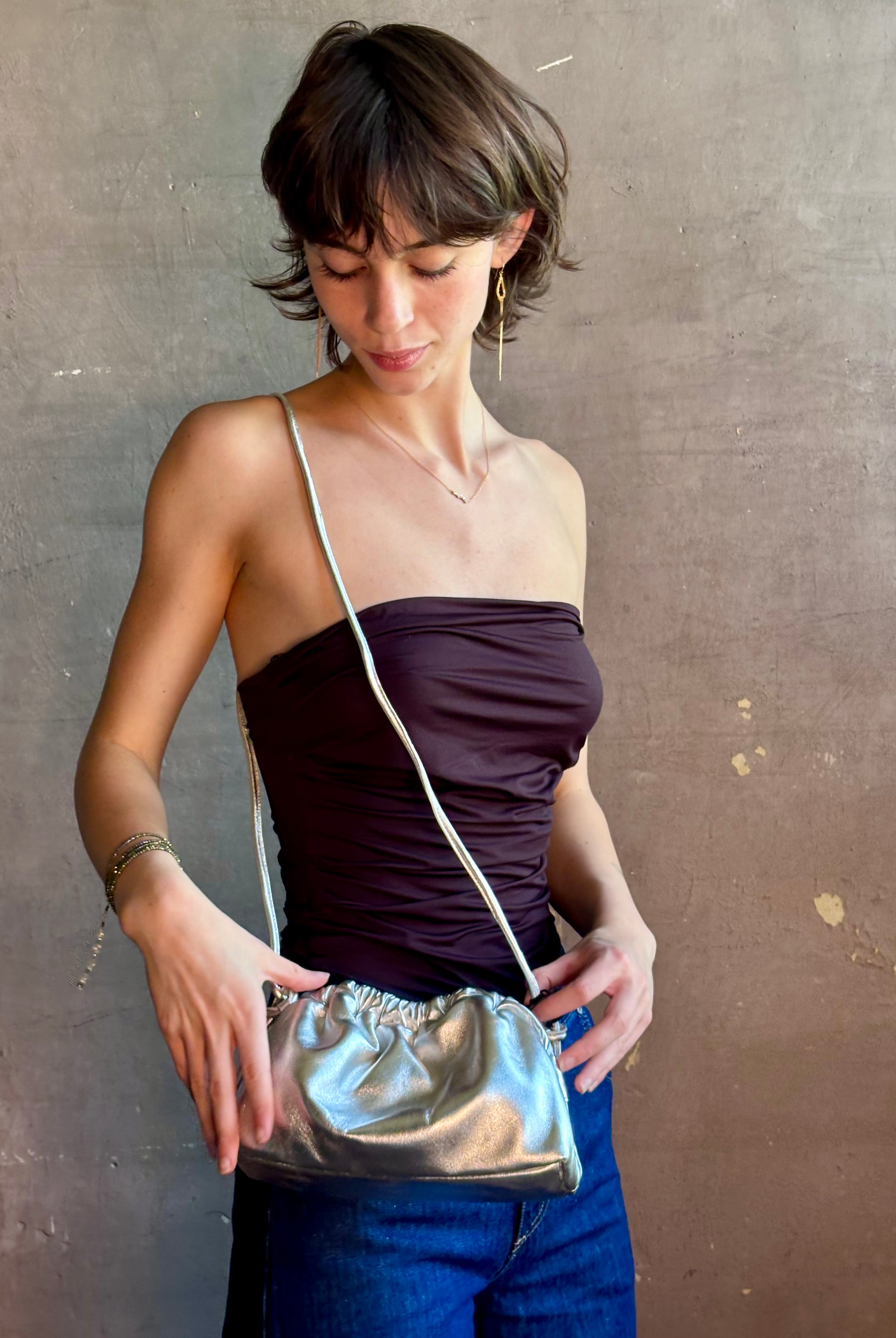 Woman wearing the Italian leather Mini Cloud crossbody by high-end designer Mansur Gavriel in metallic silver with removeable shoulder strap that can also double as a clutch
