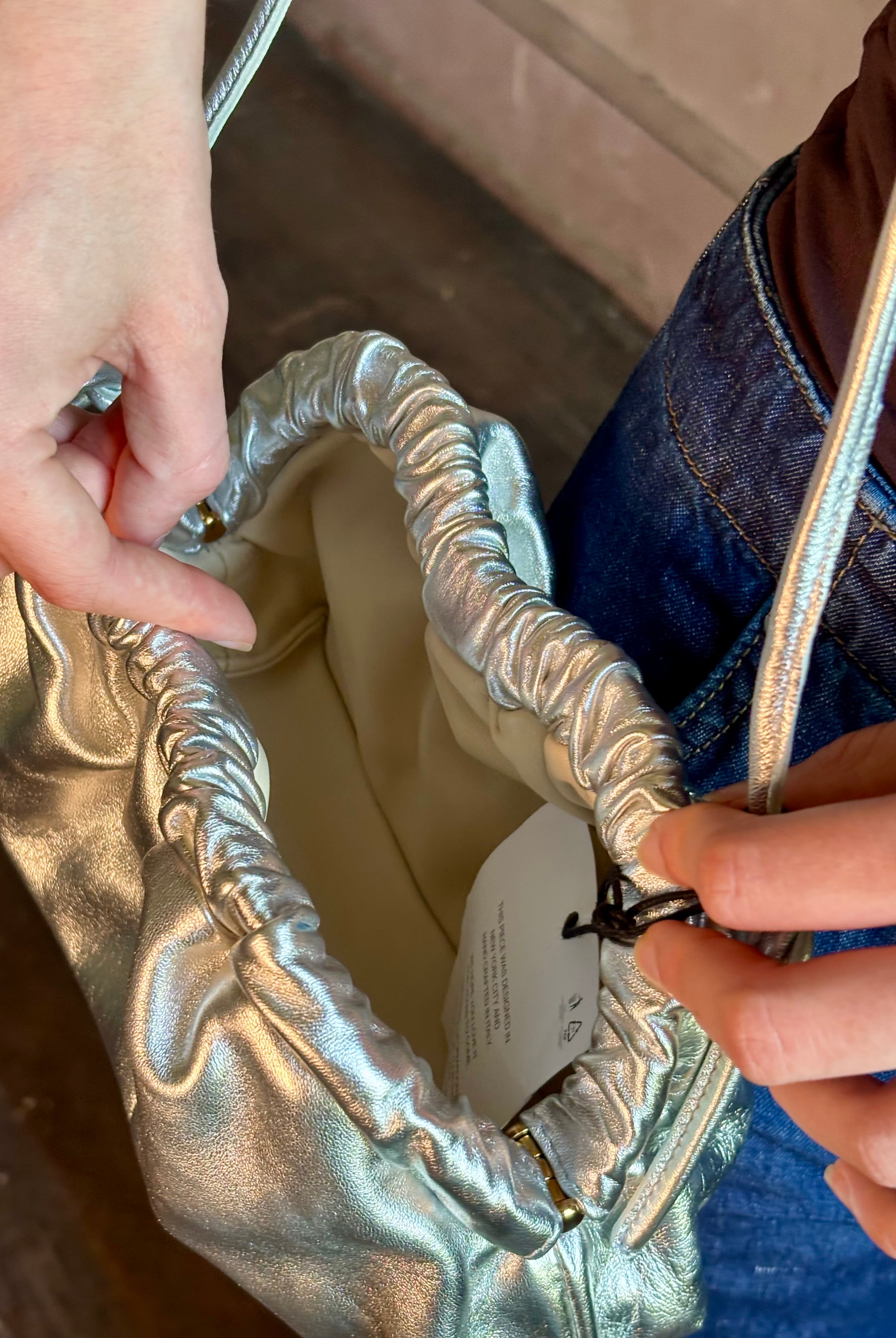 Woman wearing the Italian leather Mini Cloud crossbody by high-end designer Mansur Gavriel in metallic silver with removeable shoulder strap that can also double as a clutch