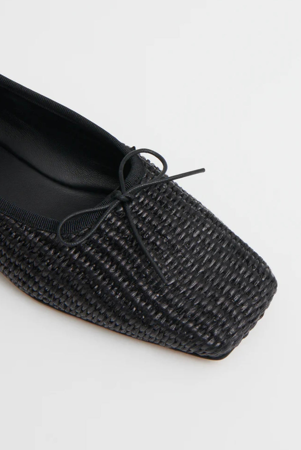 Close up image of black woven raffia ballet flats with a square toe and bowtie by high-end footwear designer Mansur