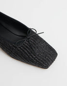 Close up image of black woven raffia ballet flats with a square toe and bowtie by high-end footwear designer Mansur