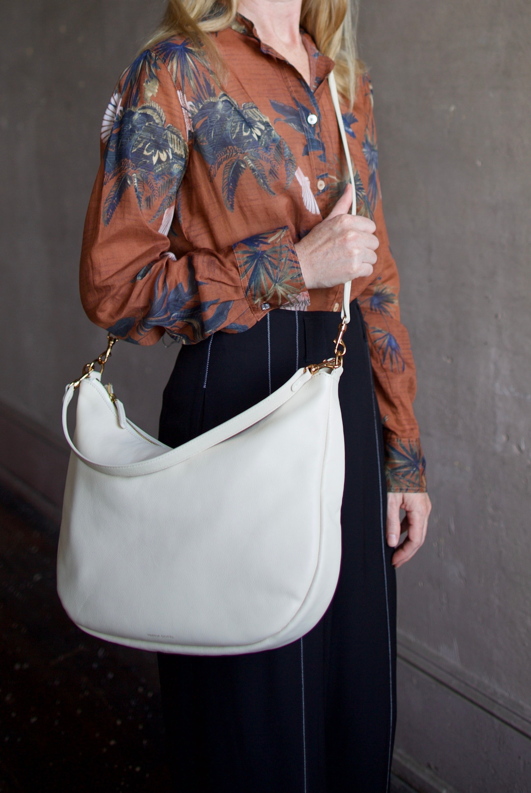 Mature model wearing the Swing Bag by High-end designer Mansur Gavriel in cream color with gold finish hardware
