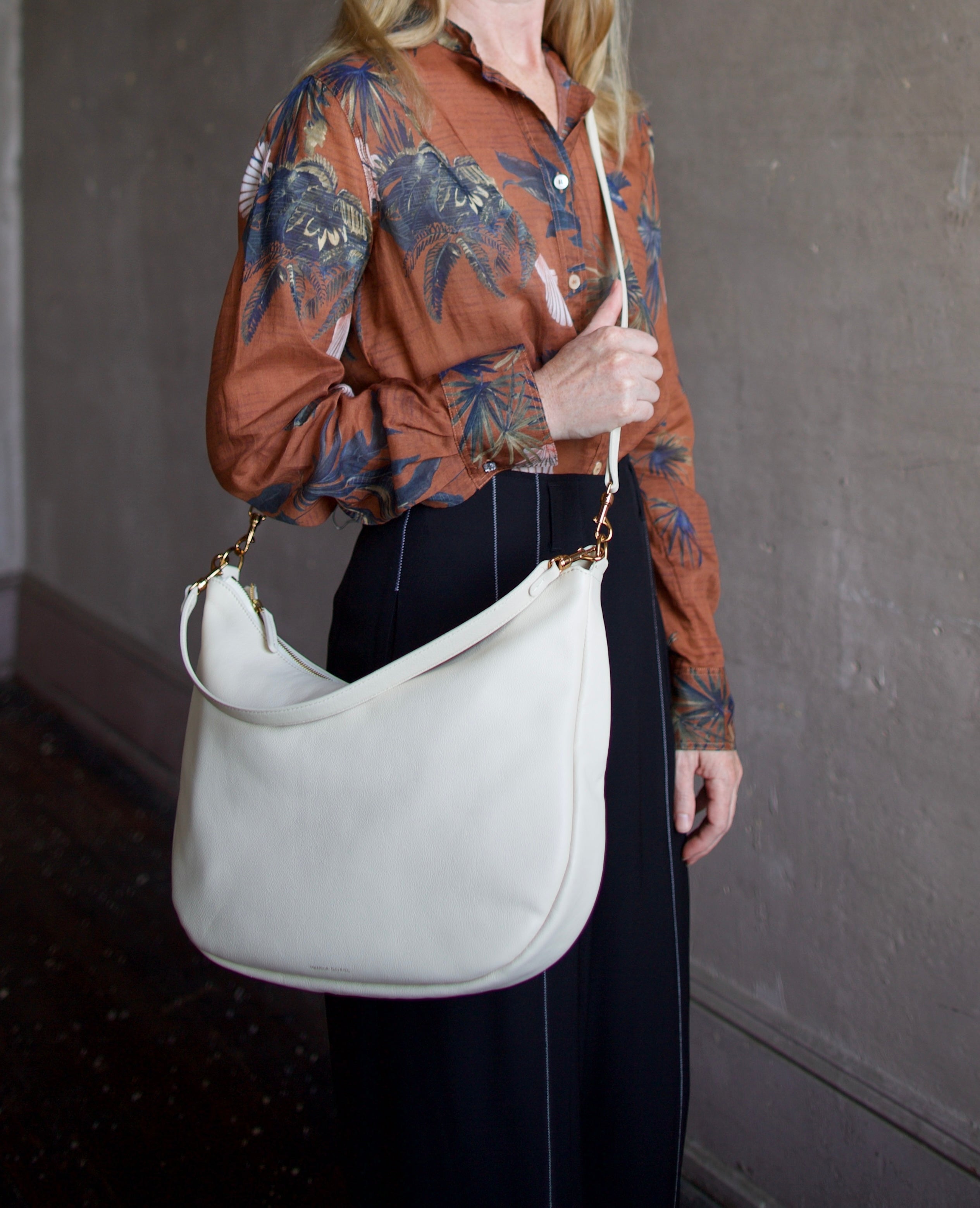 Mature model wearing the Swing Bag by High-end designer Mansur Gavriel in cream color with gold finish hardware
